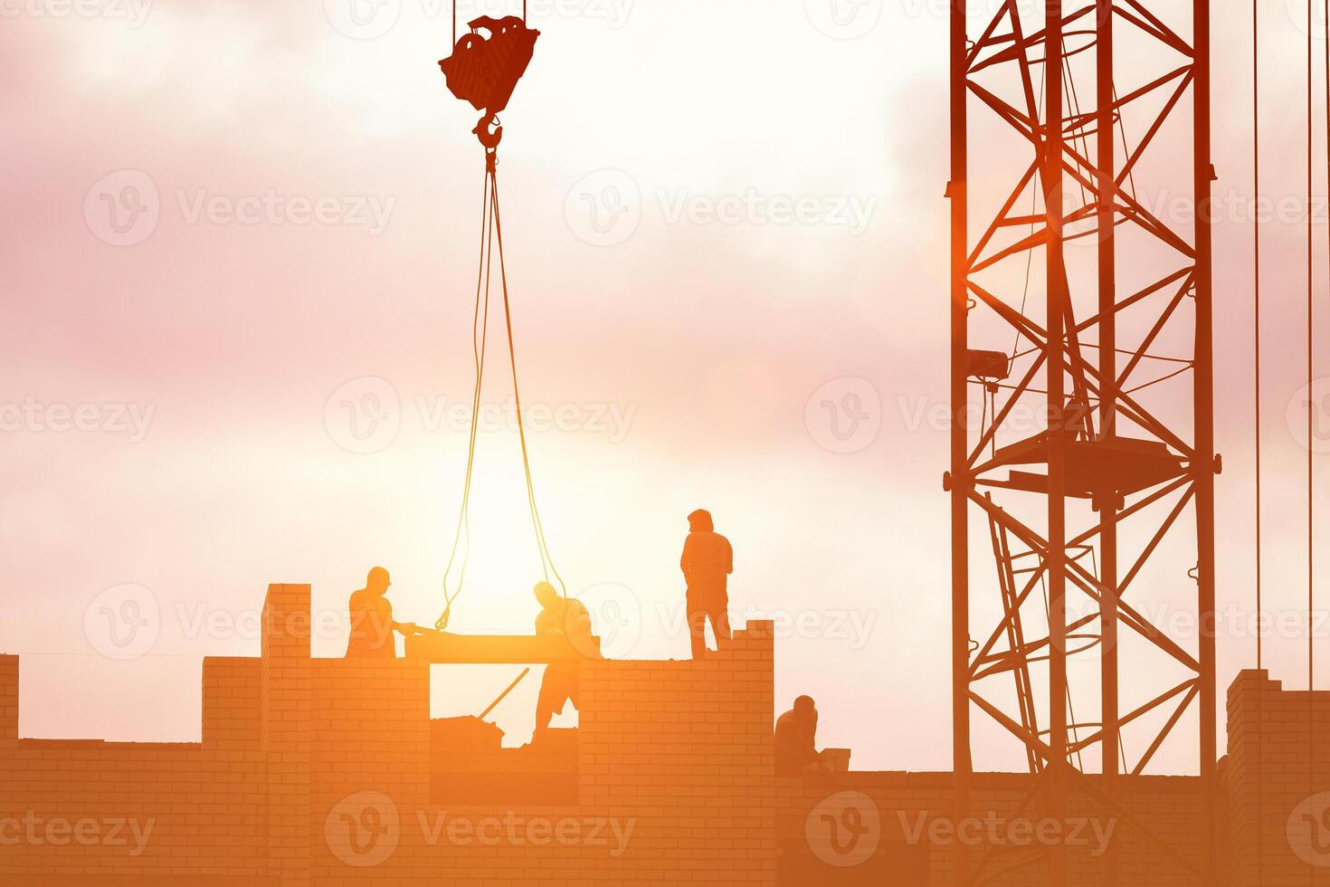 Silhouette of a team of construction workers in and a crane constructing a building on the background of the sunset sky. photo