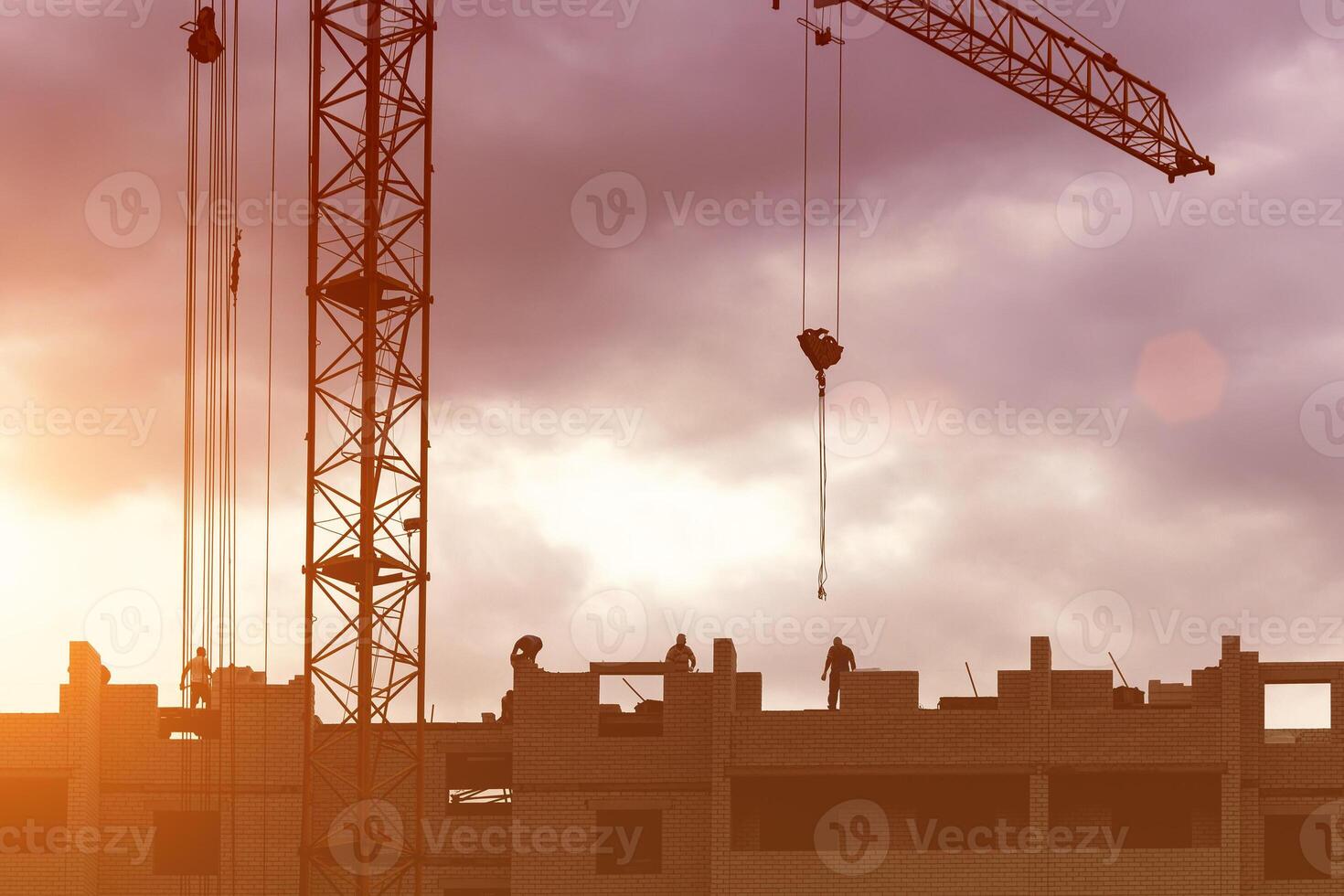 Silhouette of a team of construction workers in and a crane constructing a building on the background of the sunset sky. photo