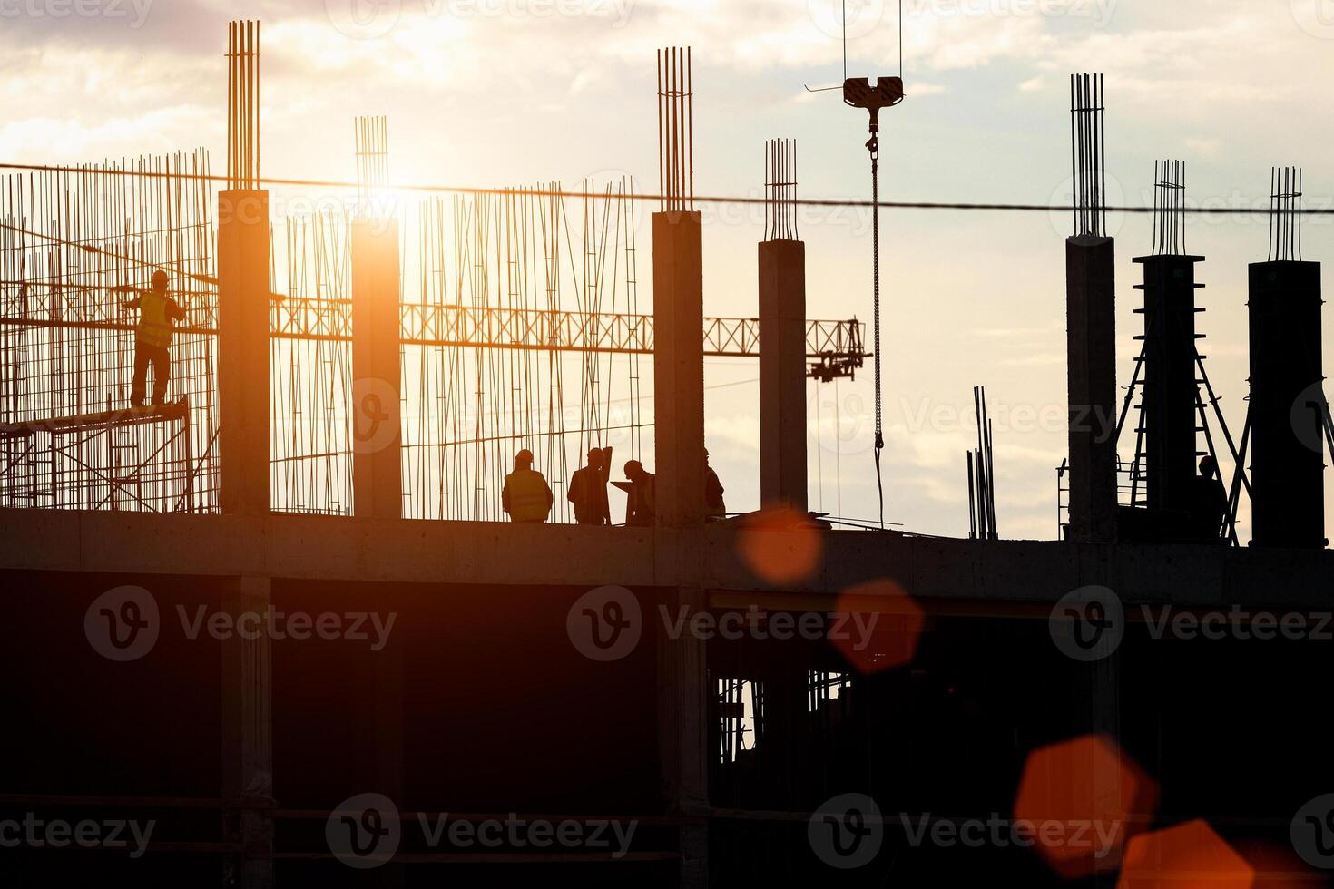Silhouette of a team of construction workers in and a crane constructing a building on the background of the sunset sky. photo