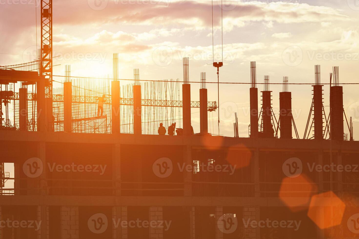 Silhouette of a team of construction workers in and a crane constructing a building on the background of the sunset sky. photo