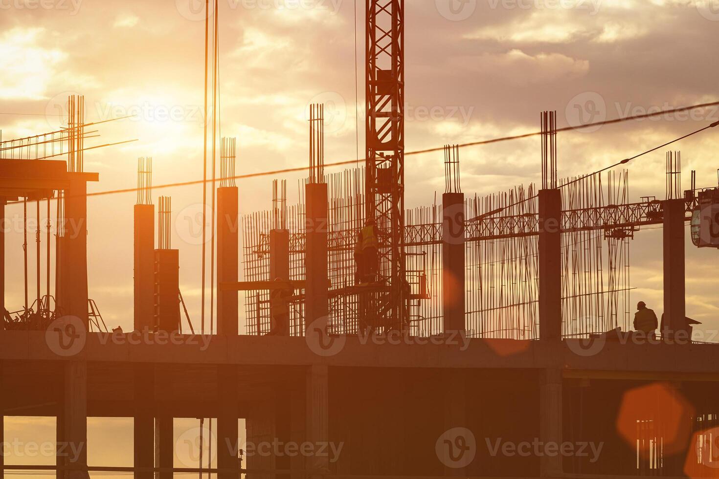 Silhouette of a team of construction workers in and a crane constructing a building on the background of the sunset sky. photo