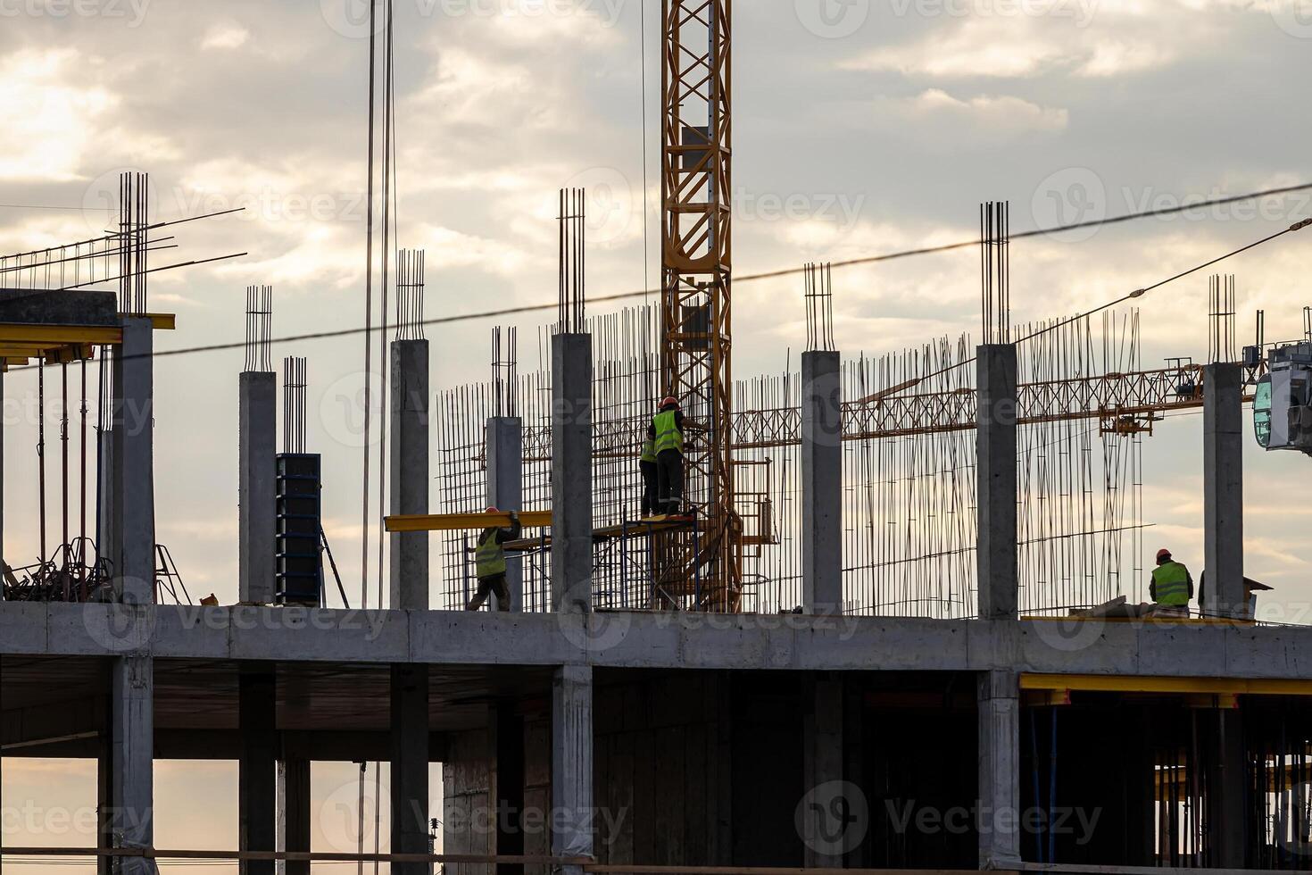 A team of construction workers in and a crane constructing a building on the background of the evening cloudy sky. photo