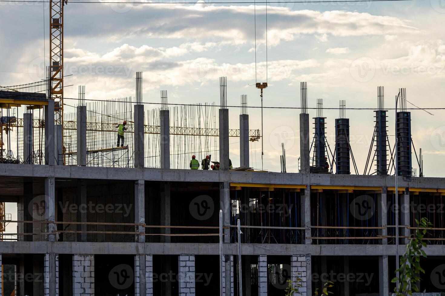 A team of construction workers in and a crane constructing a building on the background of the evening cloudy sky. photo