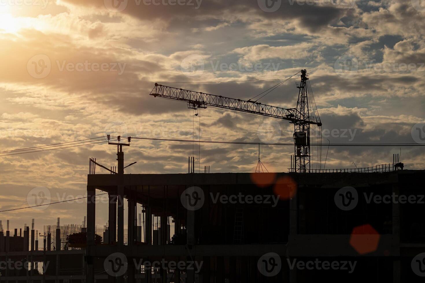 Silhouette of a team of construction workers in and a crane constructing a building on the background of the sunset sky. photo