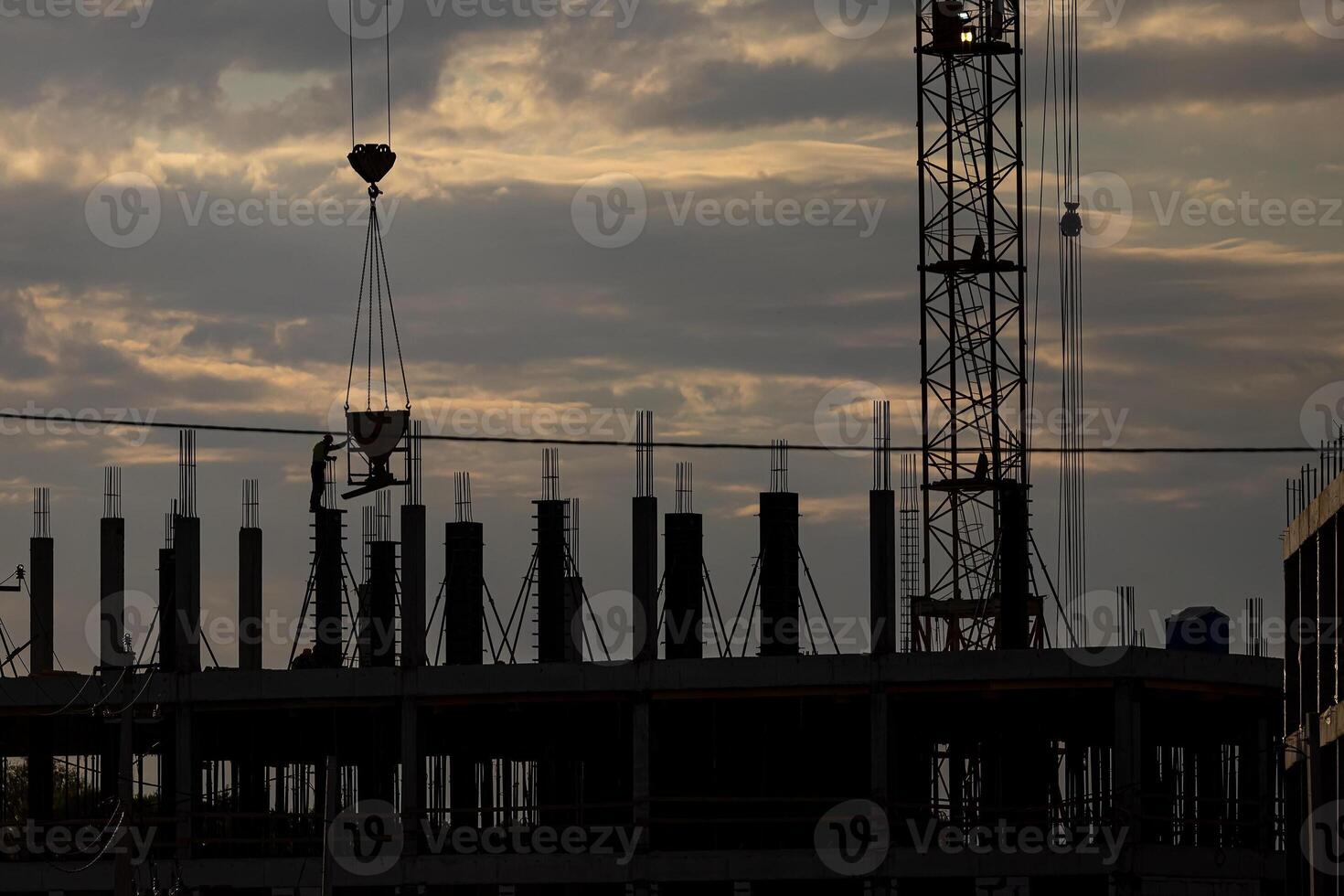 Silhouette of a team of construction workers in and a crane constructing a building on the background of the sunset sky. photo