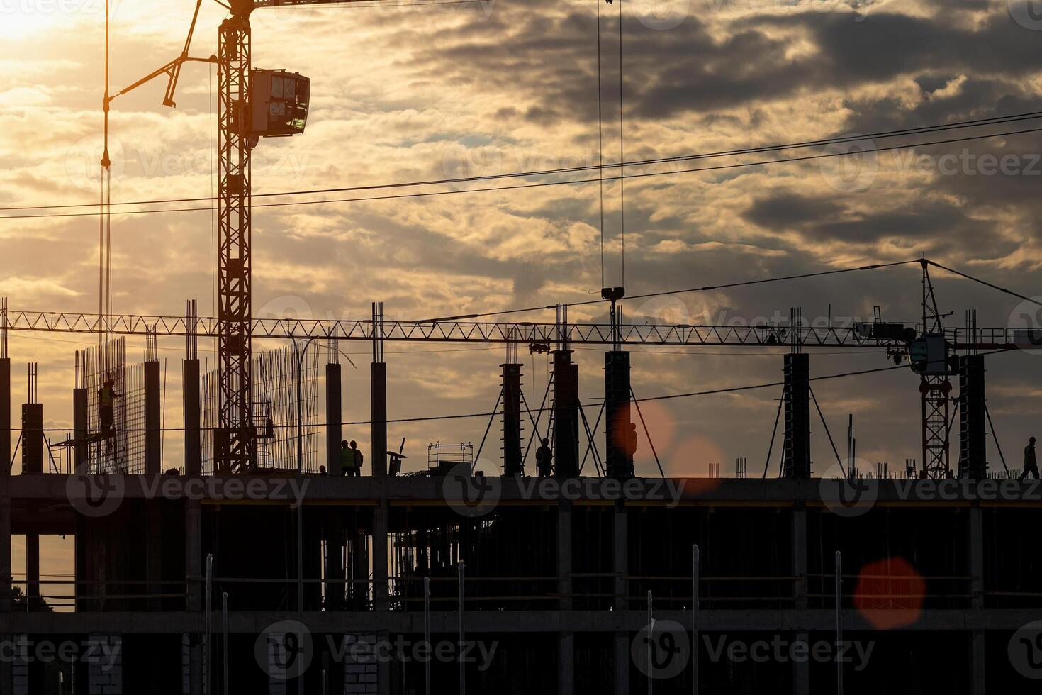 Silhouette of a team of construction workers in and a crane constructing a building on the background of the sunset sky. photo