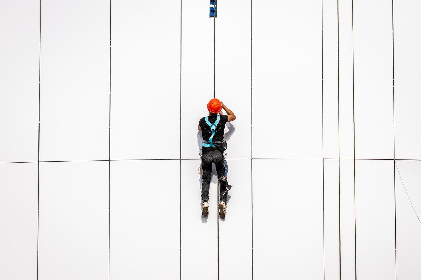 Russia, Kaluga - SEPTEMBER 16, 2020 An industrial climber hanging from a rope with a carabiner and securing the white cladding panels of a building at a construction site. photo