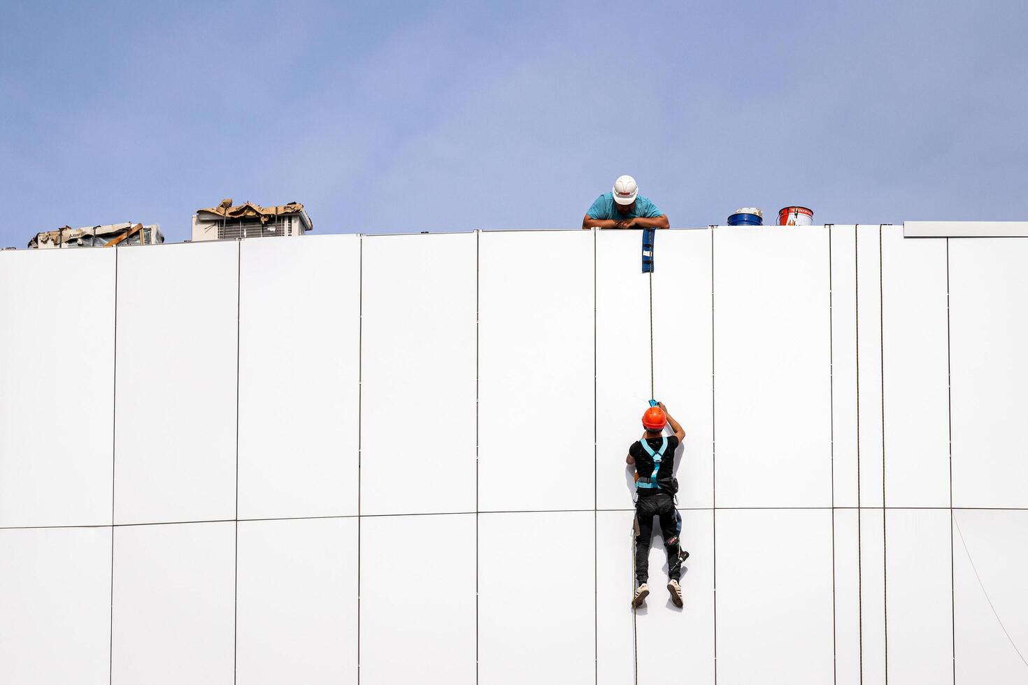 Russia, Kaluga - SEPTEMBER 16, 2020 An industrial climber hanging from a rope with a carabiner and securing the white cladding panels of a building at a construction site. photo