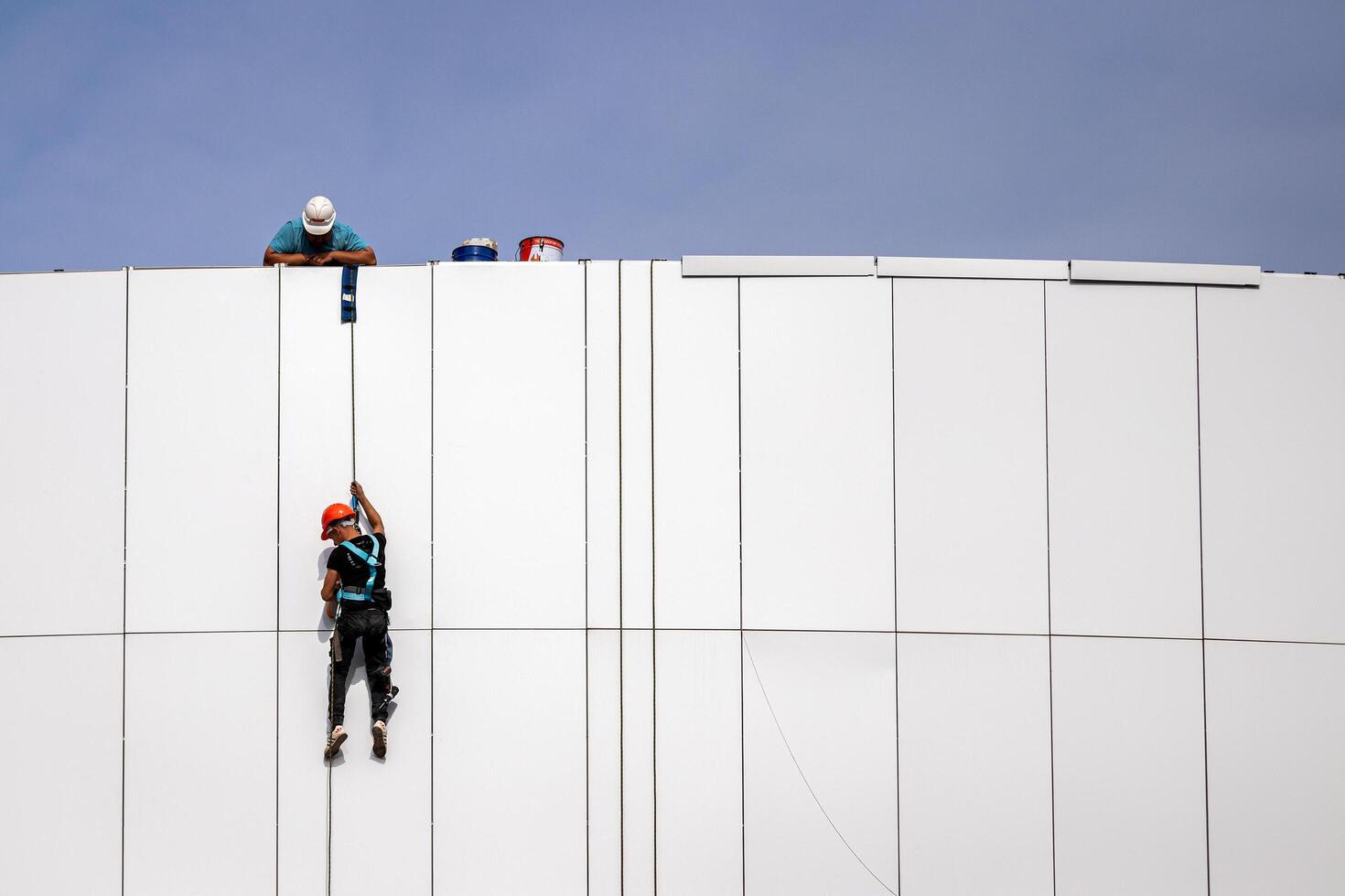 Russia, Kaluga - SEPTEMBER 16, 2020 An industrial climber hanging from a rope with a carabiner and securing the white cladding panels of a building at a construction site. photo