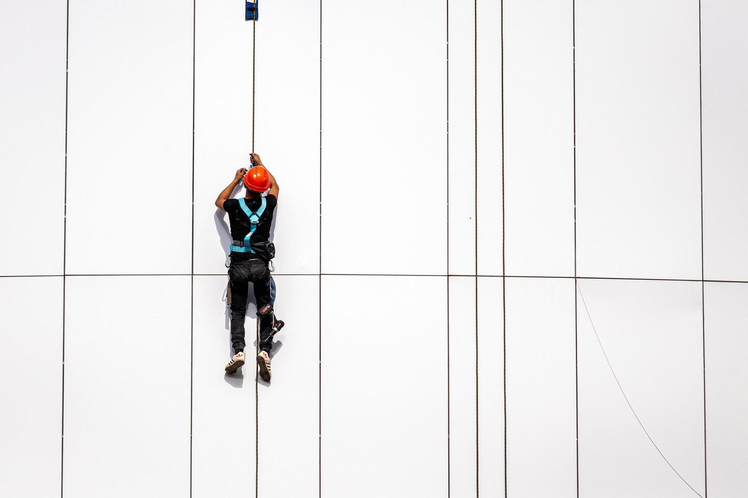 Russia, Kaluga - SEPTEMBER 16, 2020 An industrial climber hanging from a rope with a carabiner and securing the white cladding panels of a building at a construction site. photo