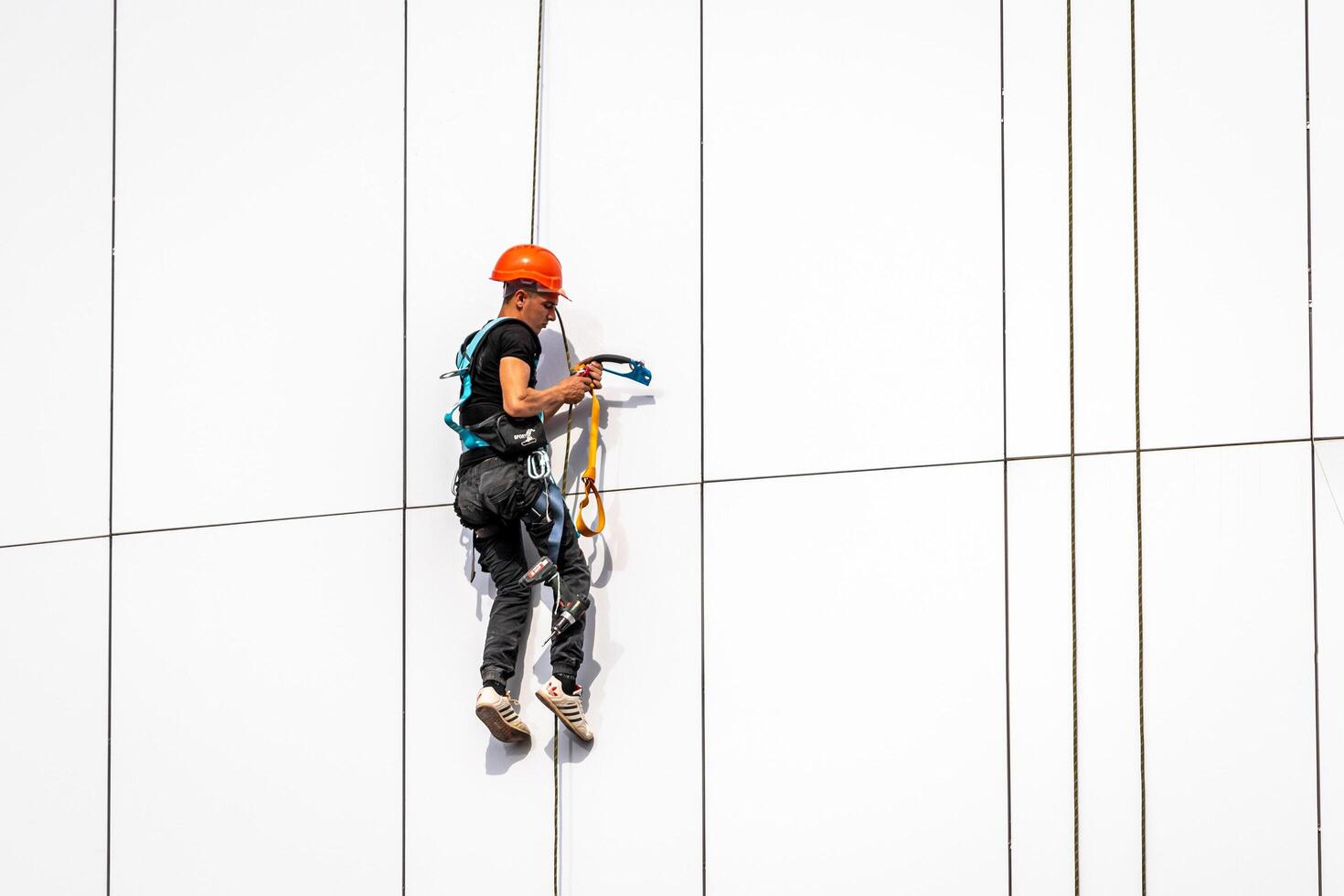 Russia, Kaluga - SEPTEMBER 16, 2020 An industrial climber hanging from a rope with a carabiner and securing the white cladding panels of a building at a construction site. photo