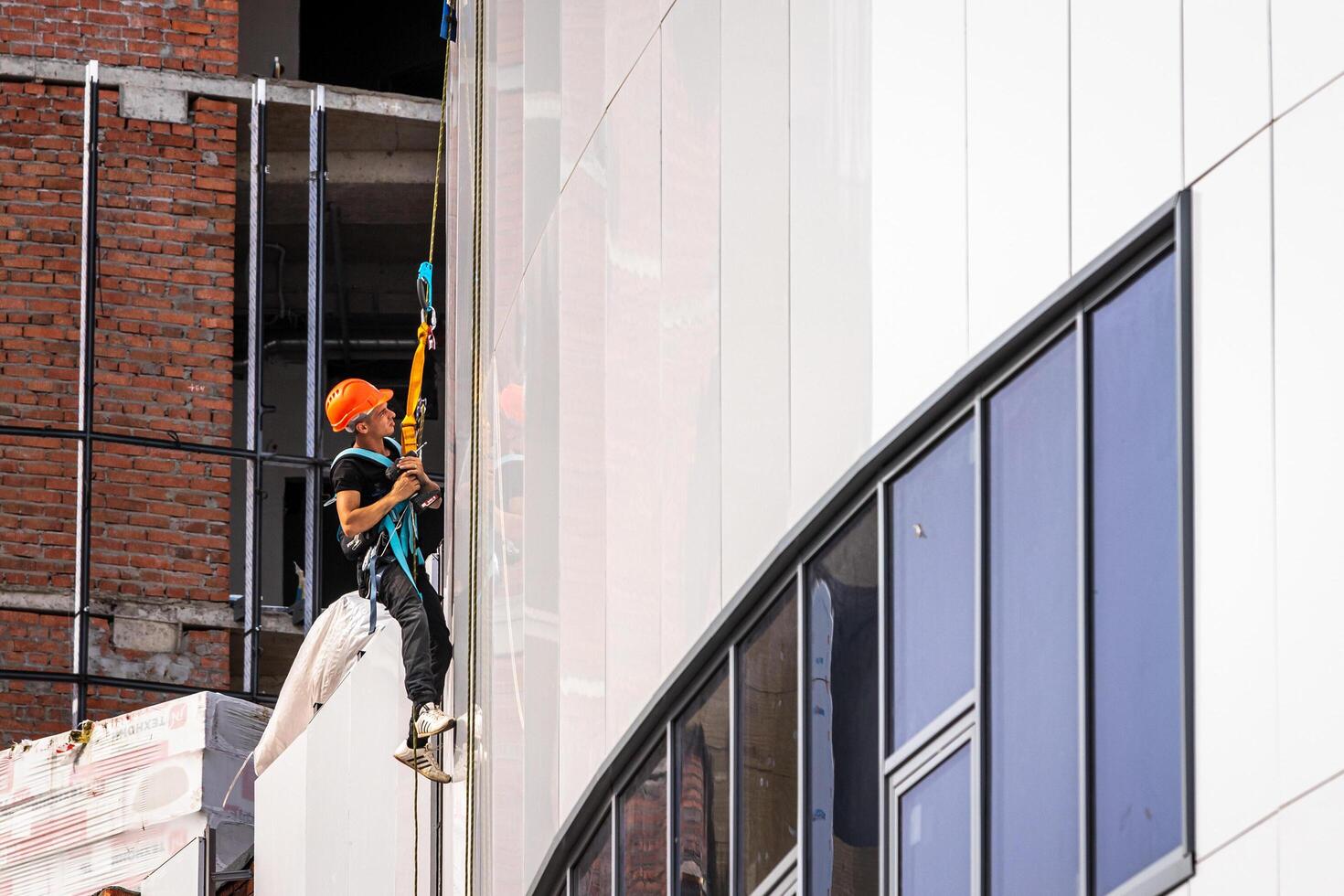 Russia, Kaluga - SEPTEMBER 16, 2020 An industrial climber hanging from a rope with a carabiner and securing the white cladding panels of a building at a construction site. photo