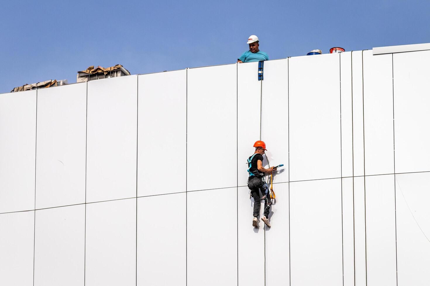 Russia, Kaluga - SEPTEMBER 16, 2020 An industrial climber hanging from a rope with a carabiner and securing the white cladding panels of a building at a construction site. photo