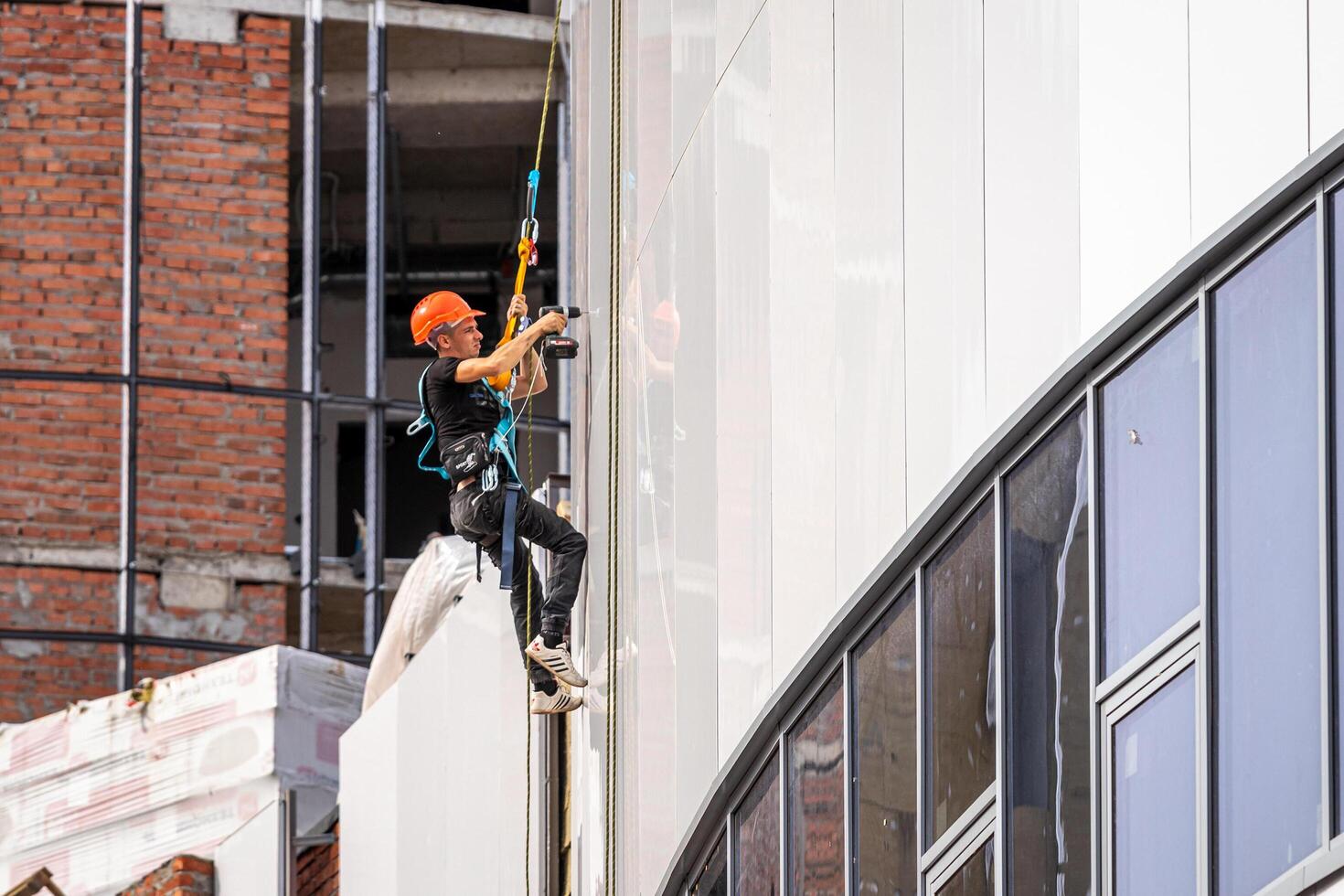 Russia, Kaluga - SEPTEMBER 16, 2020 An industrial climber hanging from a rope with a carabiner and securing the white cladding panels of a building at a construction site. photo
