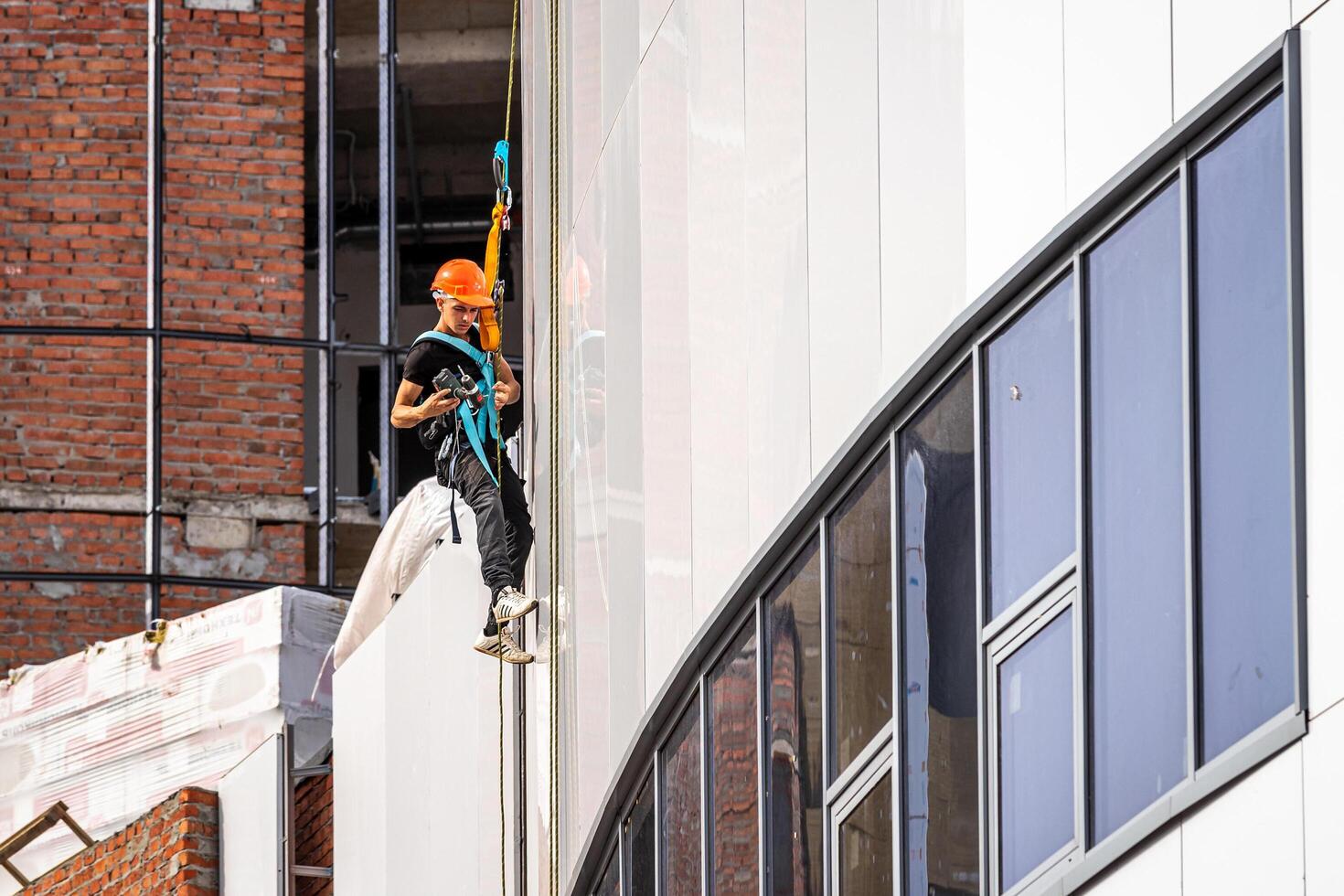 Russia, Kaluga - SEPTEMBER 16, 2020 An industrial climber hanging from a rope with a carabiner and securing the white cladding panels of a building at a construction site. photo