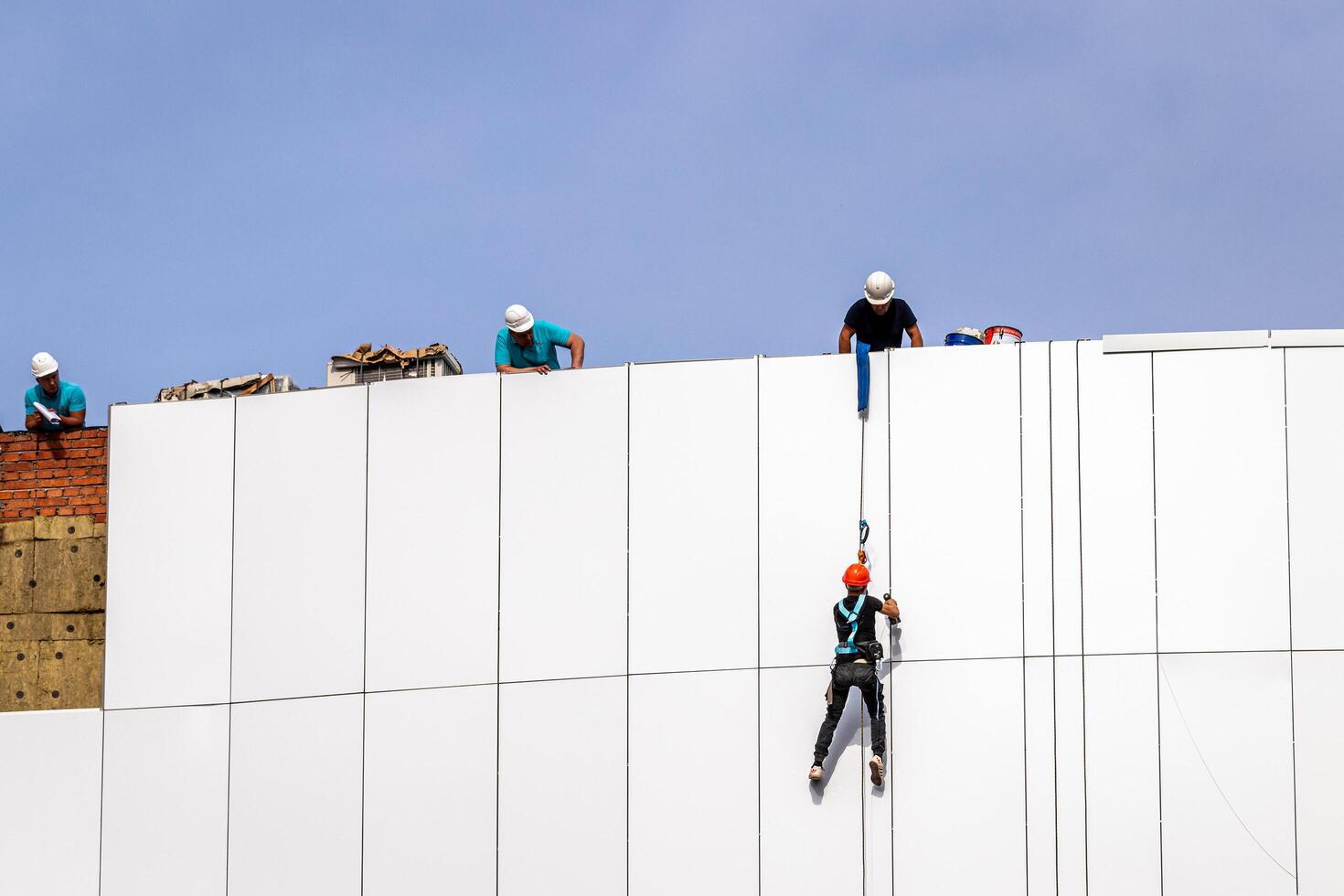 Russia, Kaluga - SEPTEMBER 16, 2020 An industrial climber hanging from a rope with a carabiner and securing the white cladding panels of a building at a construction site. photo
