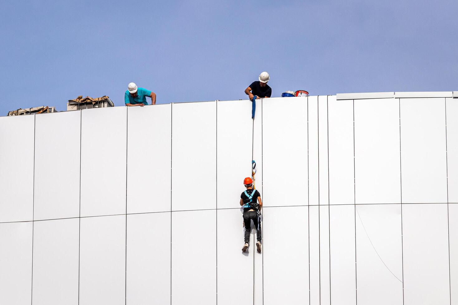 Russia, Kaluga - SEPTEMBER 16, 2020 An industrial climber hanging from a rope with a carabiner and securing the white cladding panels of a building at a construction site. photo
