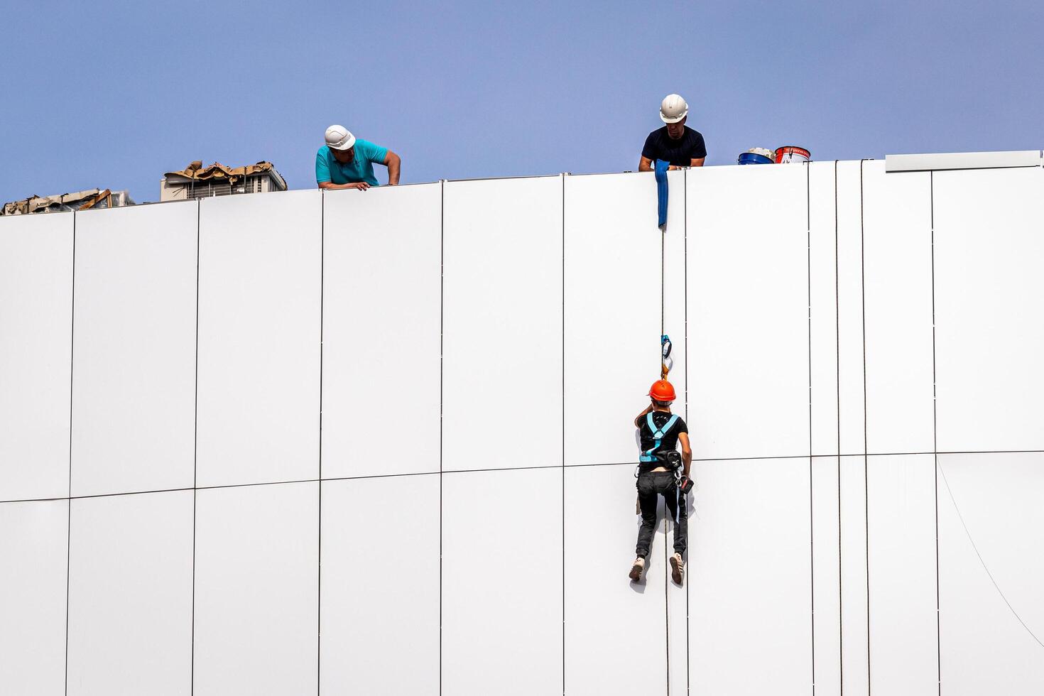 Russia, Kaluga - SEPTEMBER 16, 2020 An industrial climber hanging from a rope with a carabiner and securing the white cladding panels of a building at a construction site. photo