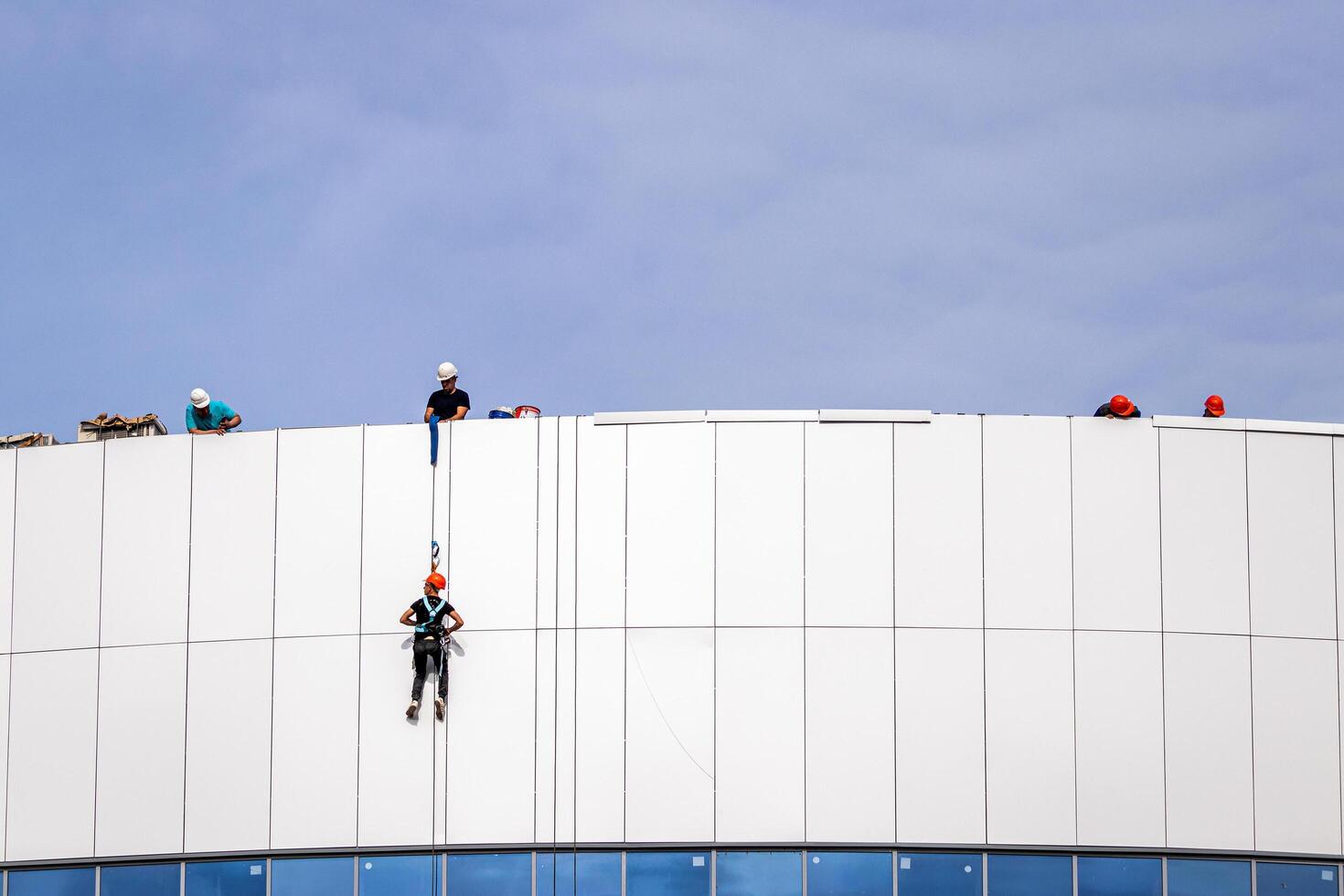 Russia, Kaluga - SEPTEMBER 16, 2020 An industrial climber hanging from a rope with a carabiner and securing the white cladding panels of a building at a construction site. photo