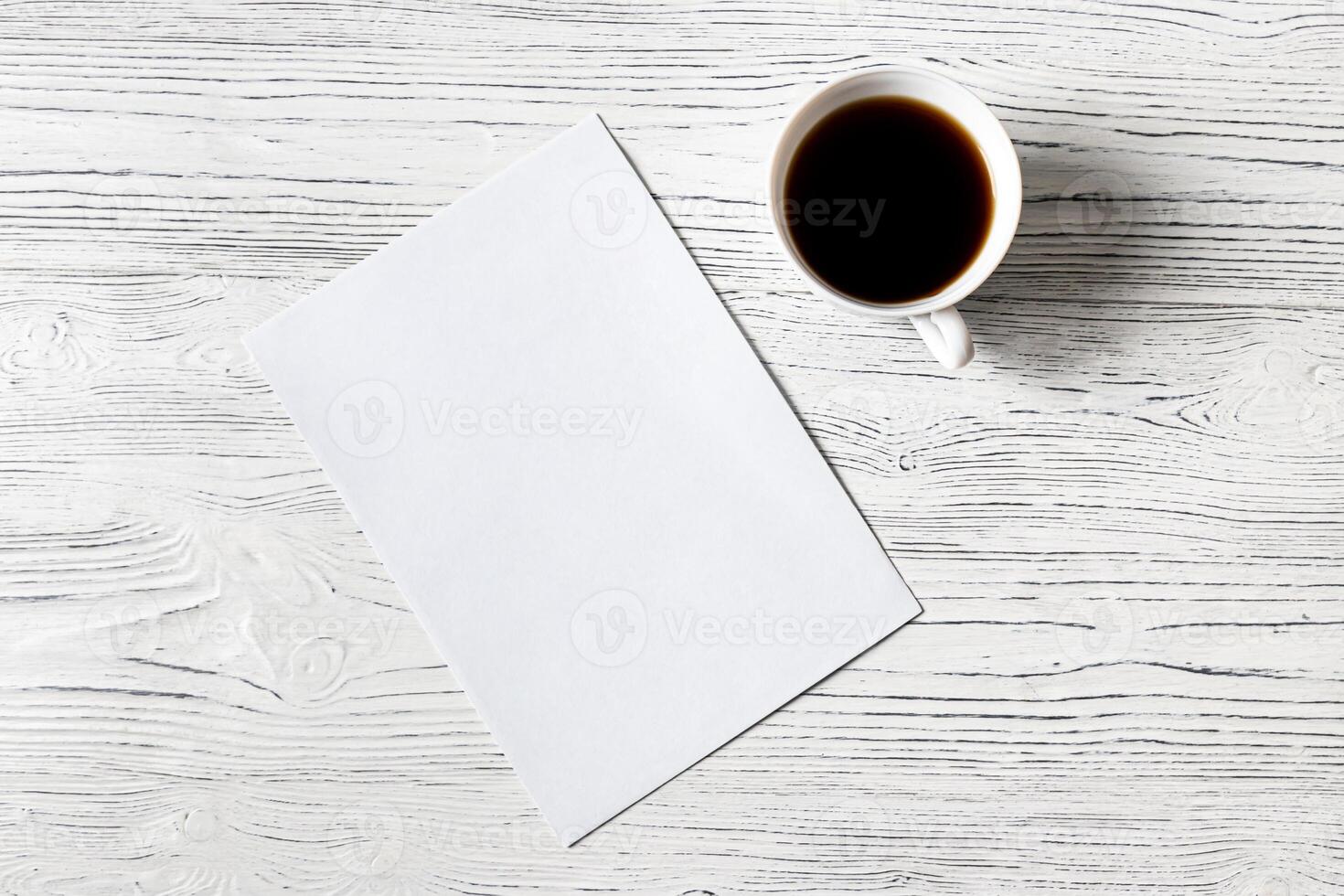 White paper sheet and cup of coffee on a wooden table. Abstract background for design. photo