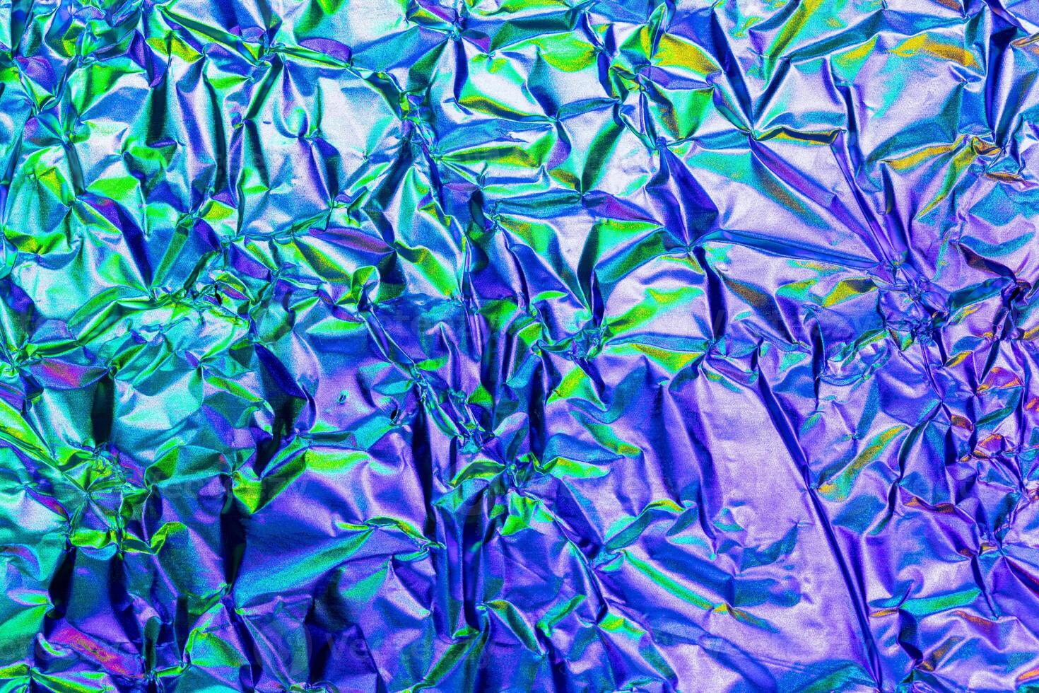 Texture of crumpled aluminum kitchen foil with reflected purple and green light. photo