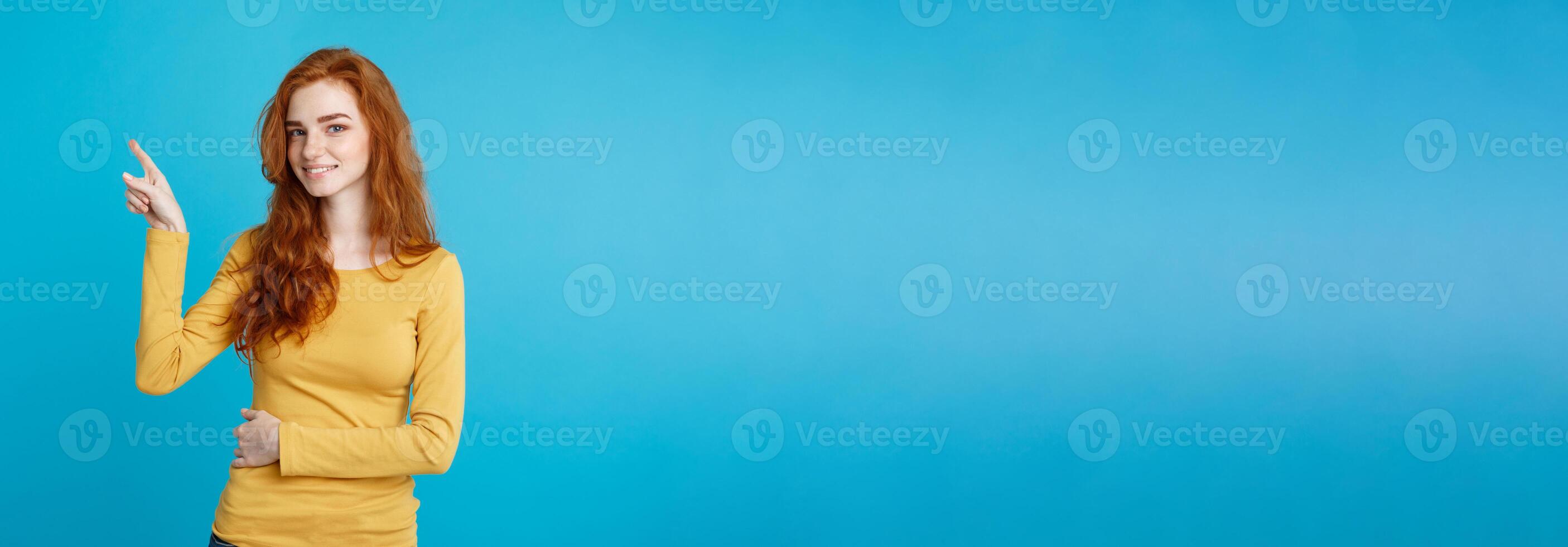 Close up Portrait young beautiful attractive redhair girl happy with something and pointing finger. Blue Pastel Background. Copy space. photo