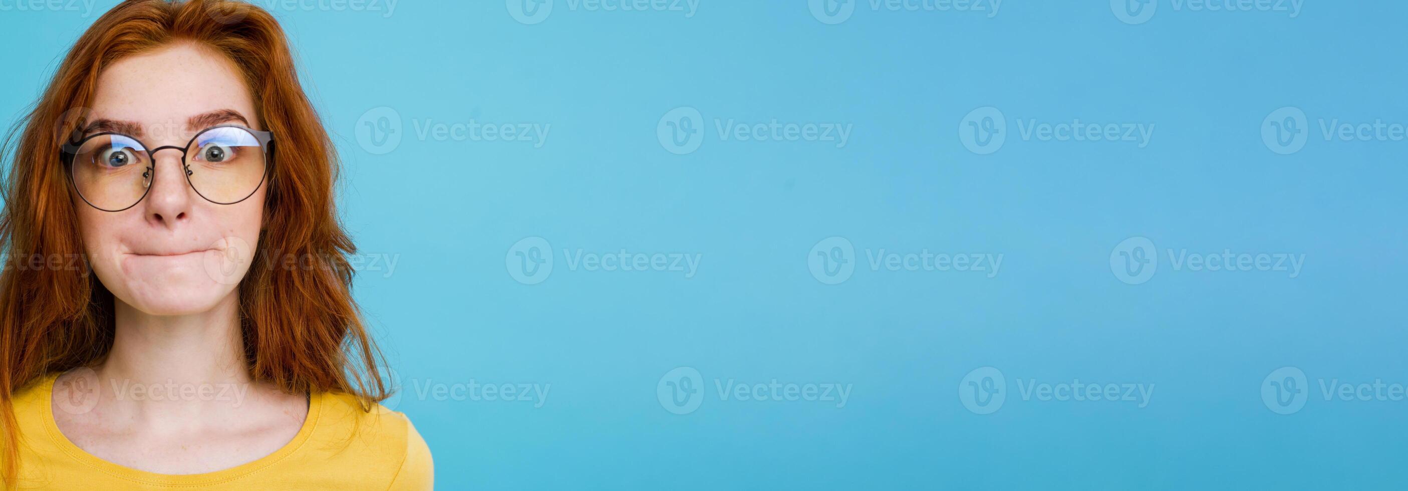 Headshot Portrait of happy ginger red hair girl with funny face looking at camera. Pastel blue background. Copy Space photo