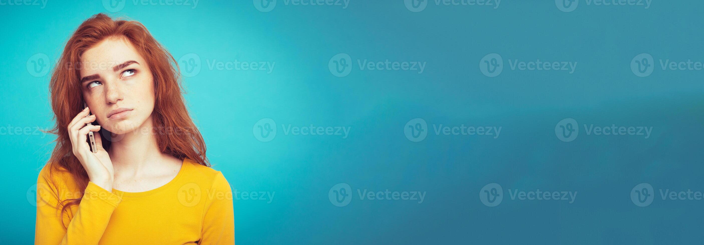 Lifestyle concept - Portrait of ginger red hair girl with shocking and stressful expression while talking with friend by mobile phone. Isolated on Blue Pastel Background. Copy space photo