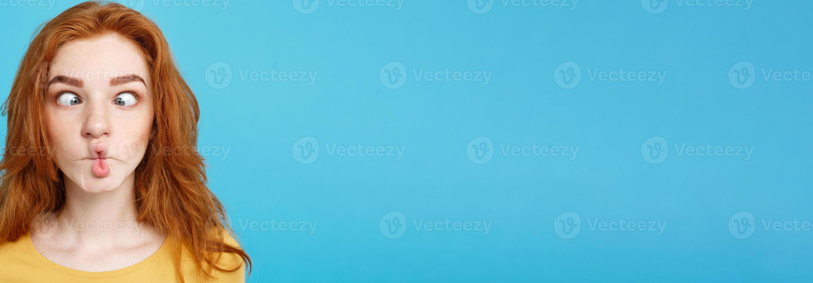 Headshot Portrait of happy ginger red hair girl with funny face looking at camera. Pastel blue background. Copy Space. photo