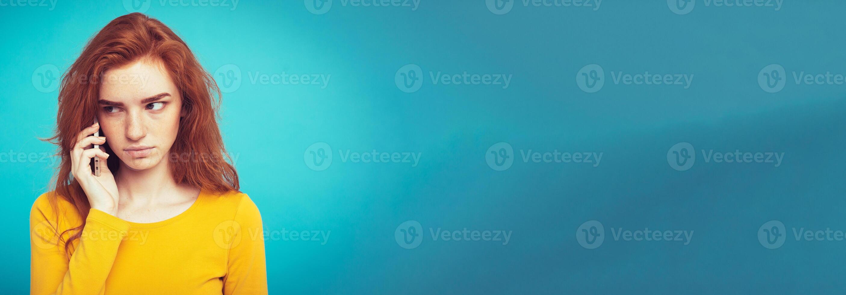 Lifestyle concept - Portrait of ginger red hair girl with shocking and stressful expression while talking with friend by mobile phone. Isolated on Blue Pastel Background. Copy space photo