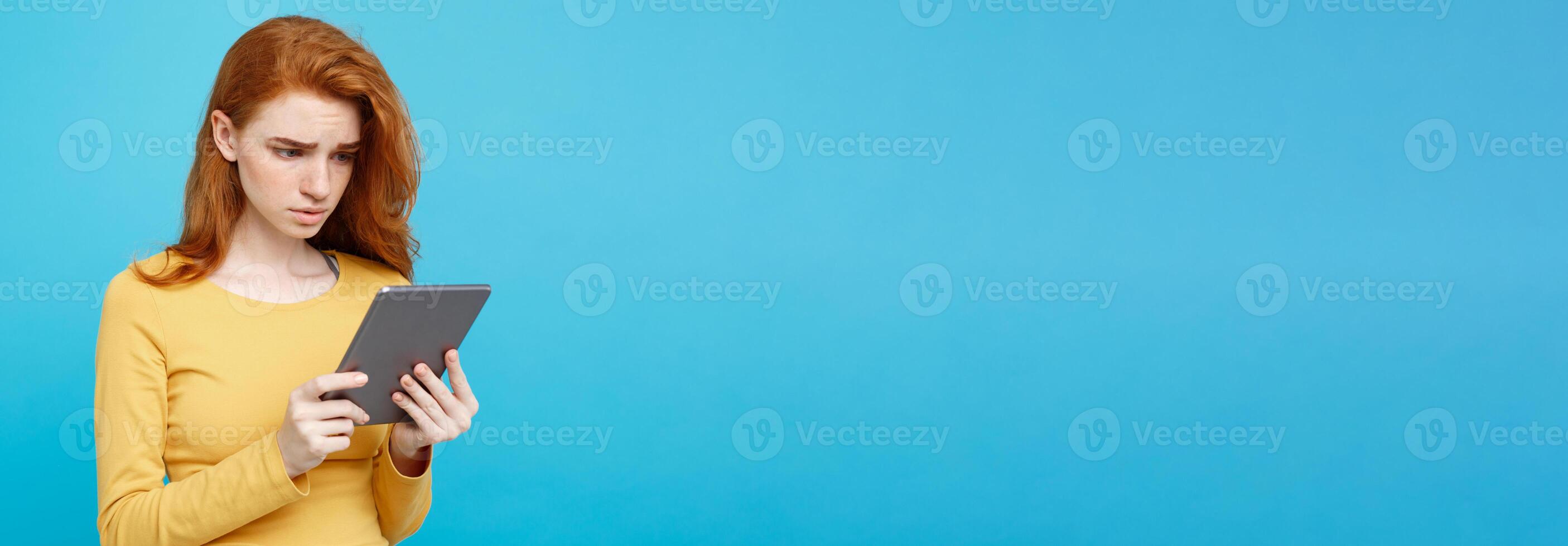 People and Technology Concept - Close up Portrait young beautiful attractive tender ginger redhair girl shocking and sad on digital table with wining something. Blue Pastel Background. Copy space. photo