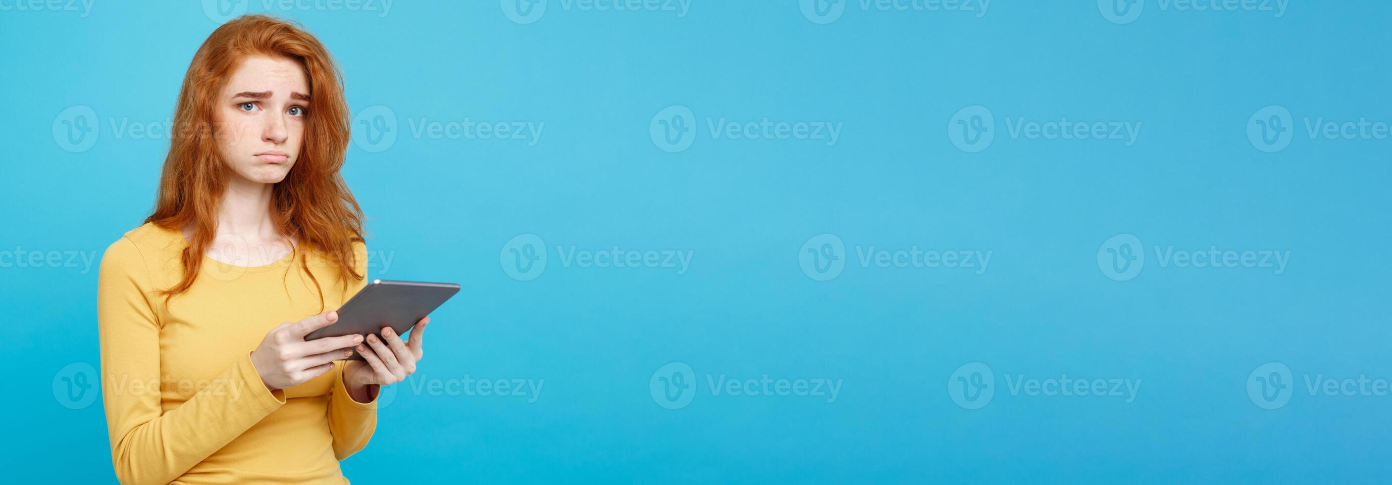 People and Technology Concept - Close up Portrait young beautiful attractive tender ginger redhair girl shocking and sad on digital table with wining something. Blue Pastel Background. Copy space. photo