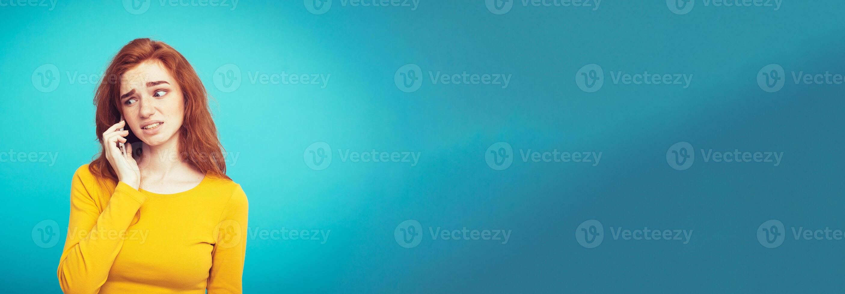 Lifestyle concept - Portrait of ginger red hair girl with shocking and stressful expression while talking with friend by mobile phone. Isolated on Blue Pastel Background. Copy space photo