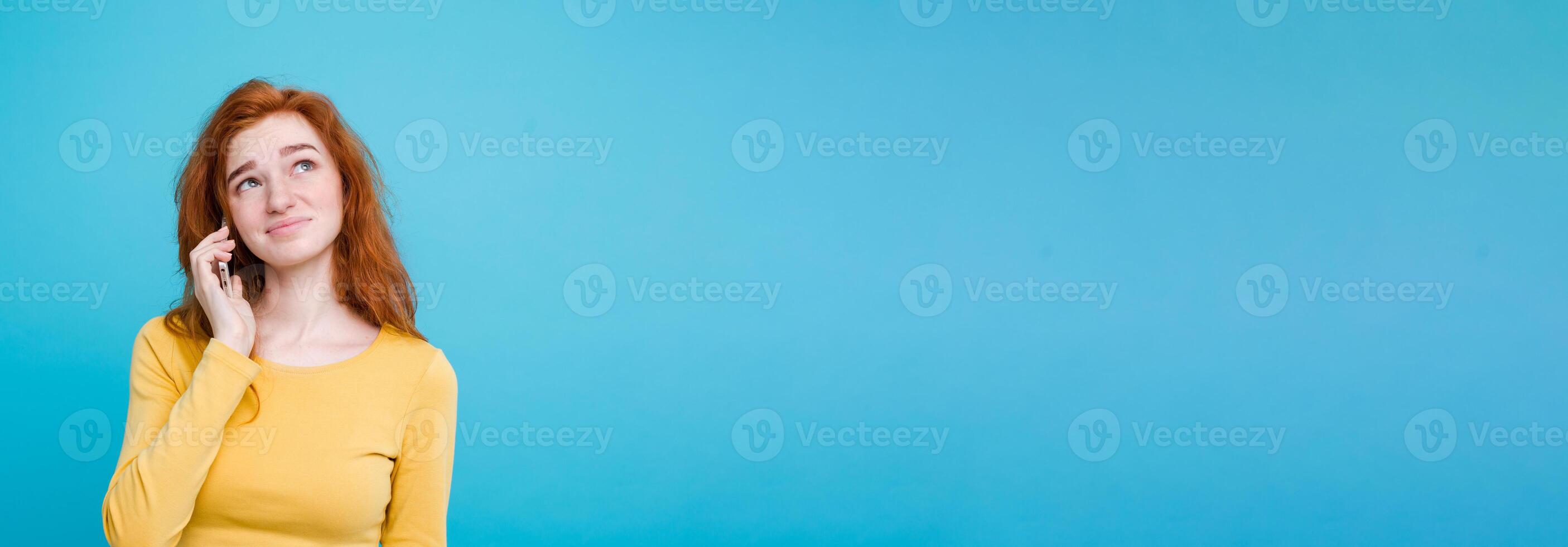 Lifestyle concept - Portrait of ginger red hair girl with shocking and stressful expression while talking with friend by mobile phone. Isolated on Blue Pastel Background. Copy space photo