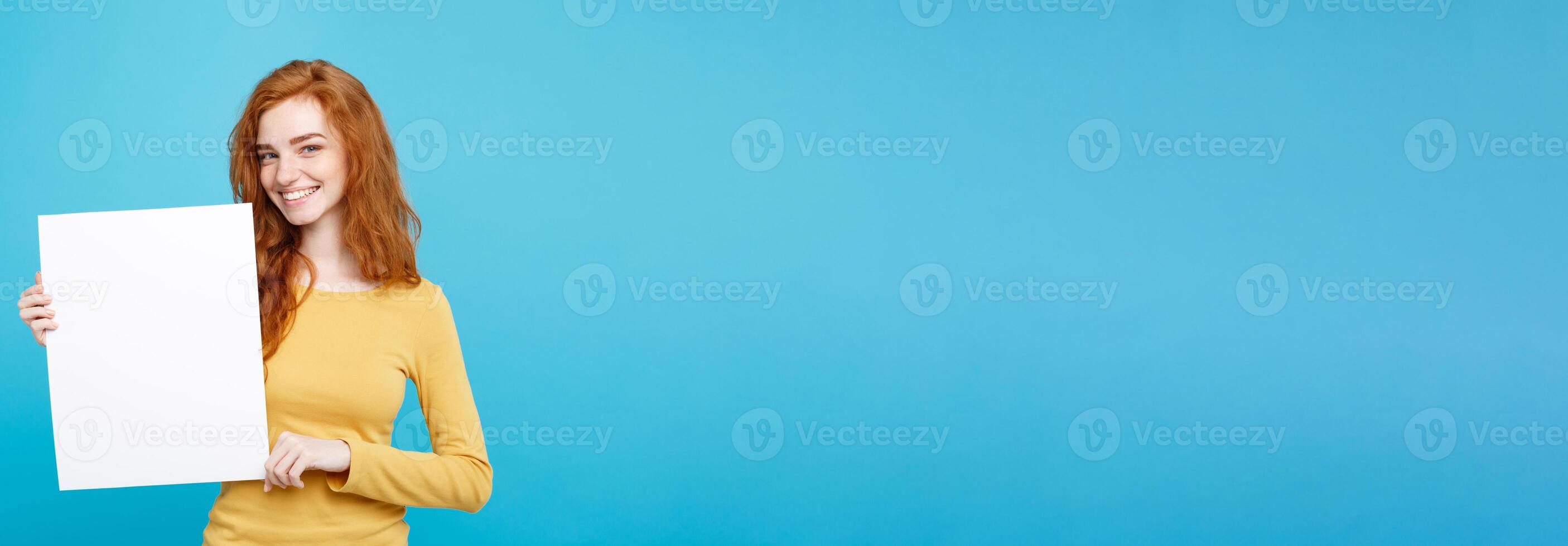 Close up Portrait young beautiful attractive ginger red hair girl smiling showing blank sign. Blue Pastel Background. Copy space. photo