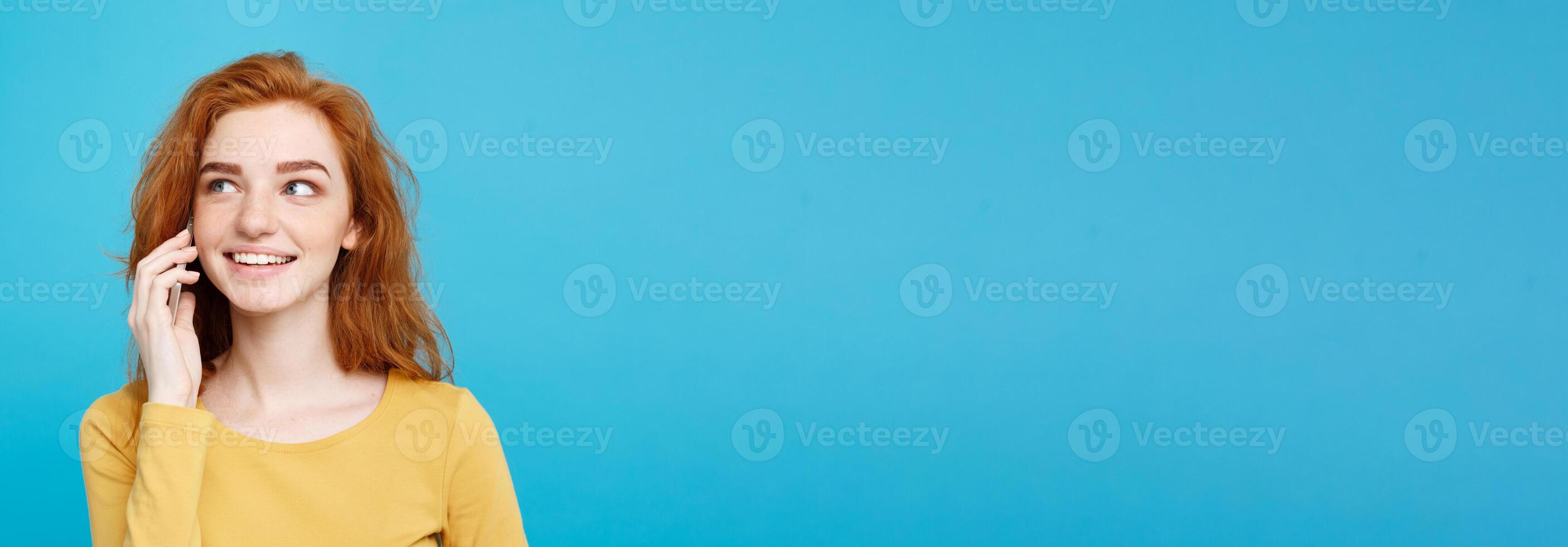 Lifestyle and Technology concept - Portrait of cheerful happy ginger red hair girl with joyful and exciting talking with friend by mobile phone. Isolated on Blue Pastel Background. Copy space. photo
