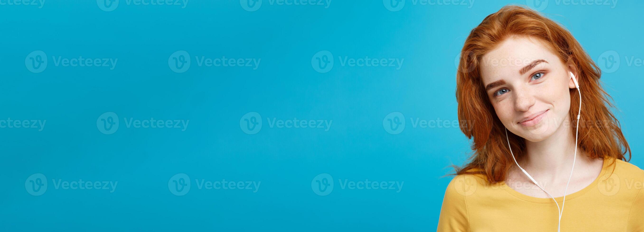Lifestyle concept - Portrait of cheerful happy ginger red hair girl enjoy listening to music with headphones joyful smiling to camera. Isolated on Blue Pastel Background. Copy space. photo