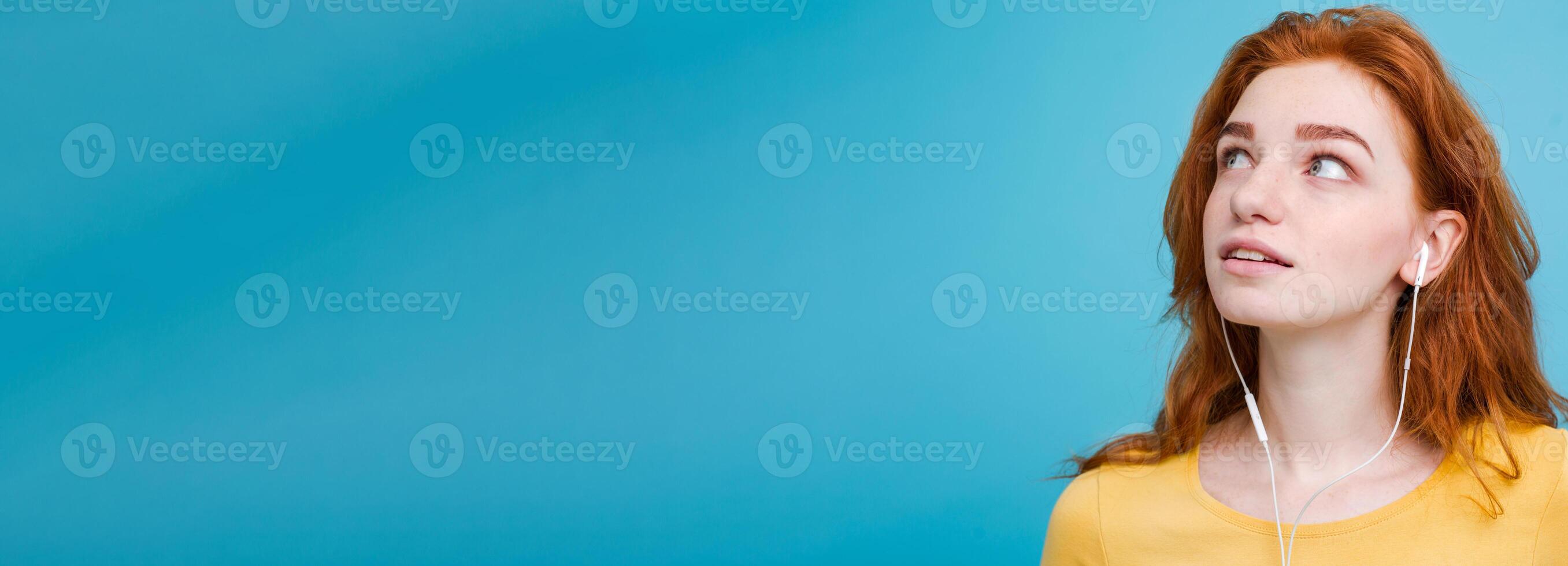 Lifestyle concept - Portrait of cheerful happy ginger red hair girl enjoy listening to music with headphones joyful smiling to camera. Isolated on Blue Pastel Background. Copy space photo