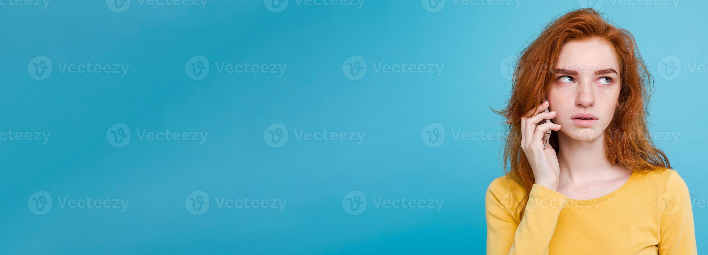 Lifestyle concept - Portrait of ginger red hair girl with shocking and stressful expression while talking with friend by mobile phone. Isolated on Blue Pastel Background. Copy space photo