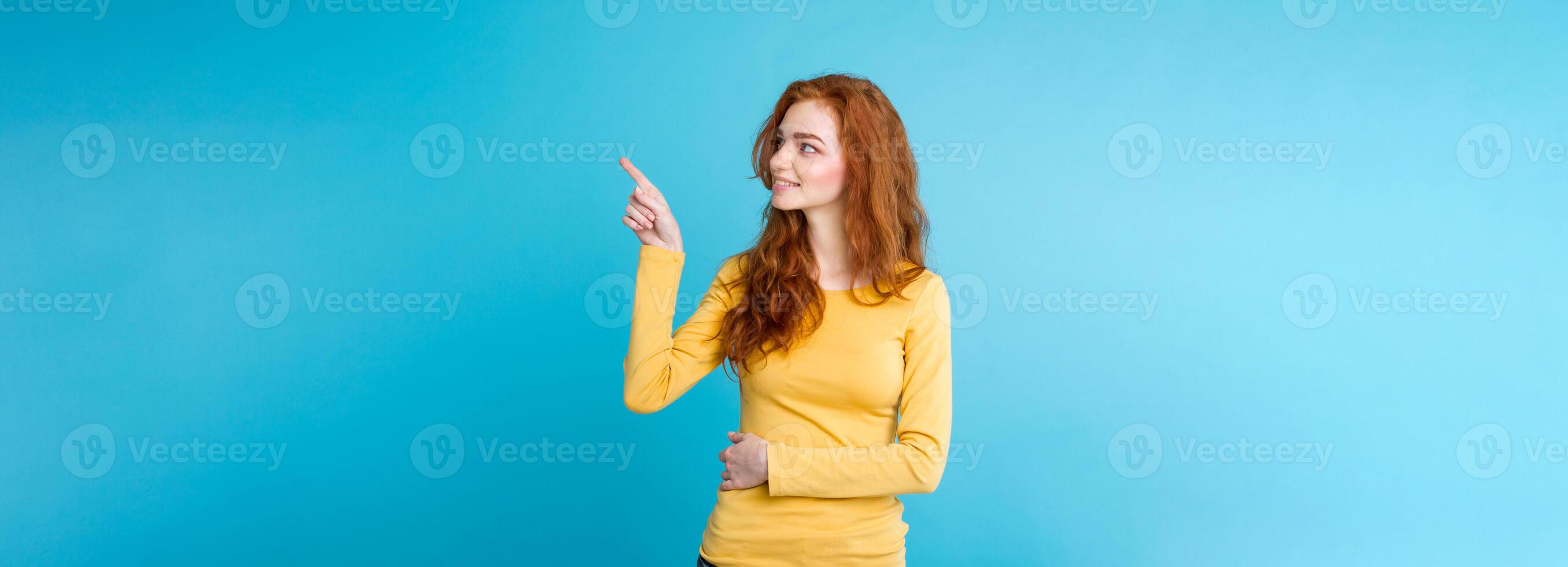 Close up Portrait young beautiful attractive redhair girl happy with something and pointing finger. Blue Pastel Background. Copy space photo