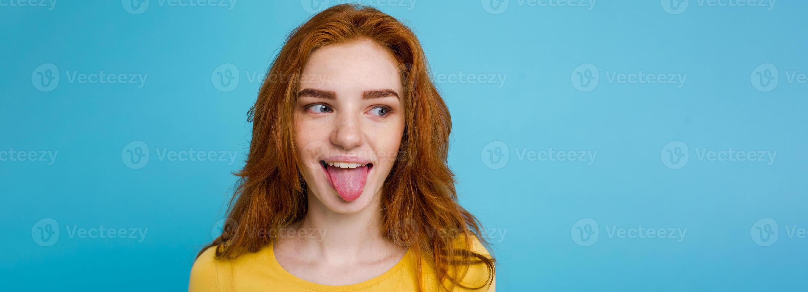 Headshot Portrait of happy ginger red hair girl with funny face looking at camera. Pastel blue background. Copy Space photo