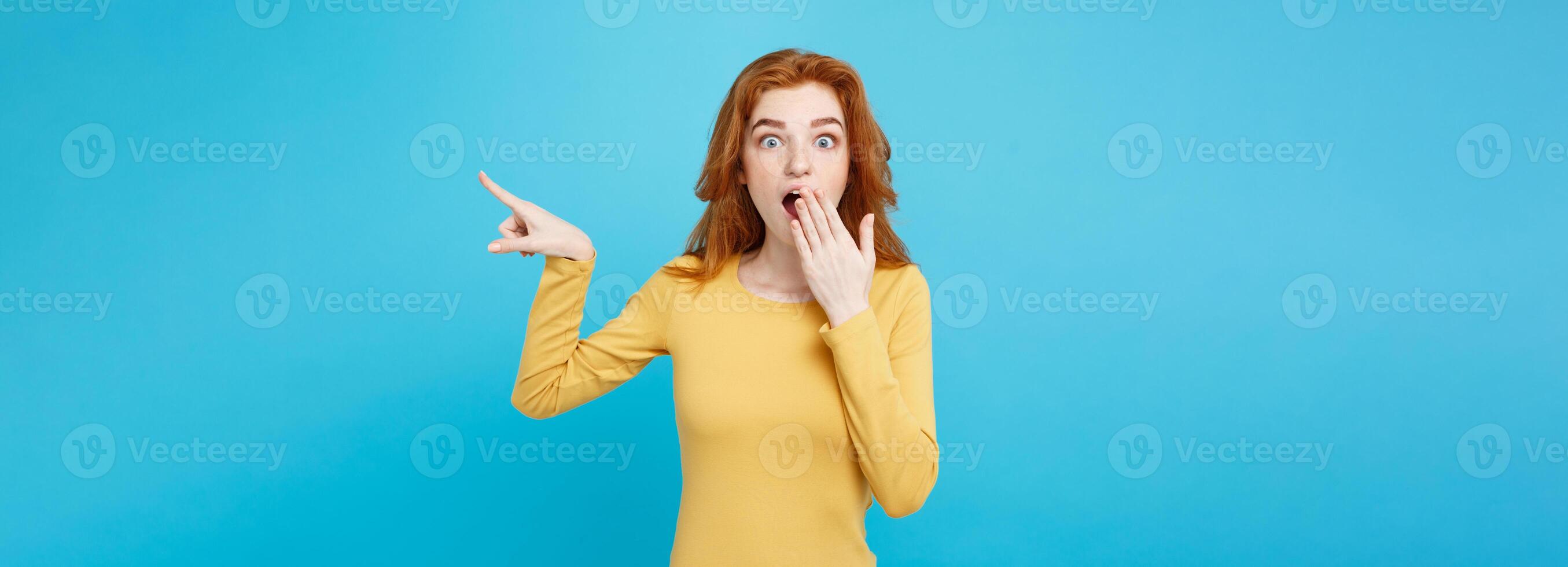 Close up Portrait young beautiful attractive redhair girl with shocking with something and pointing finger. Blue Pastel Background. Copy space. photo