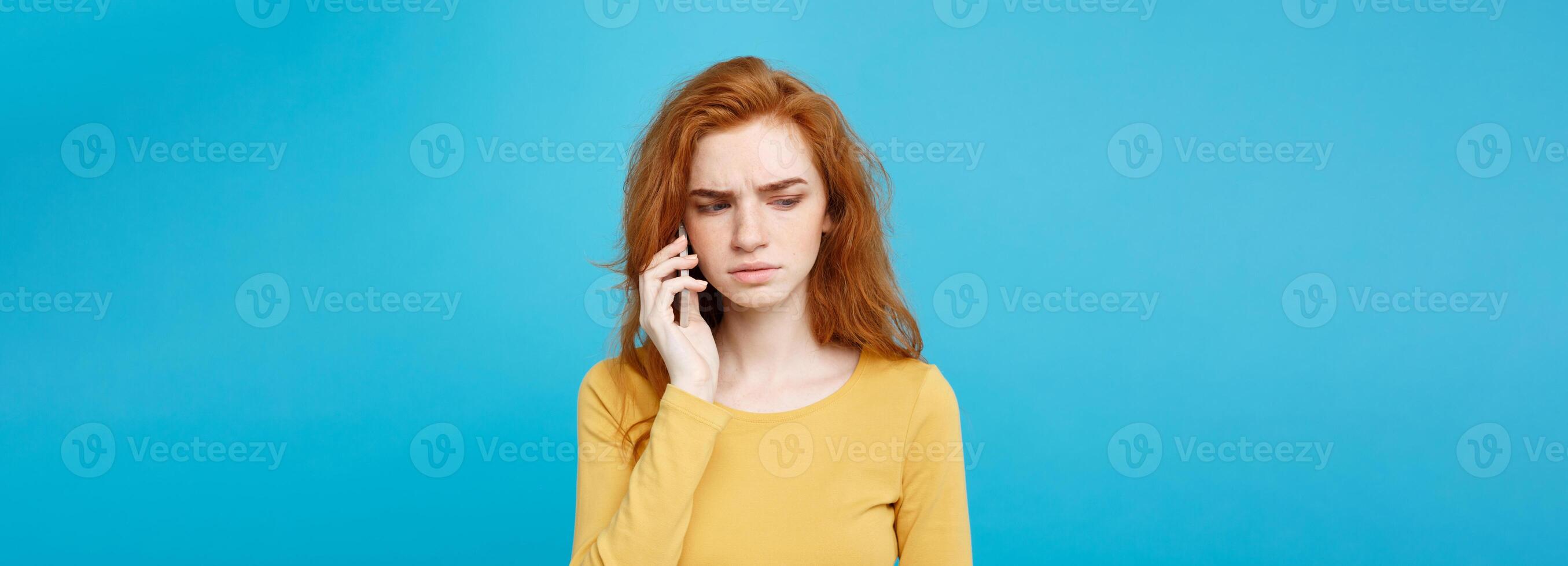 Lifestyle concept - Portrait of ginger red hair girl with shocking and stressful expression while talking with friend by mobile phone. Isolated on Blue Pastel Background. Copy space. photo
