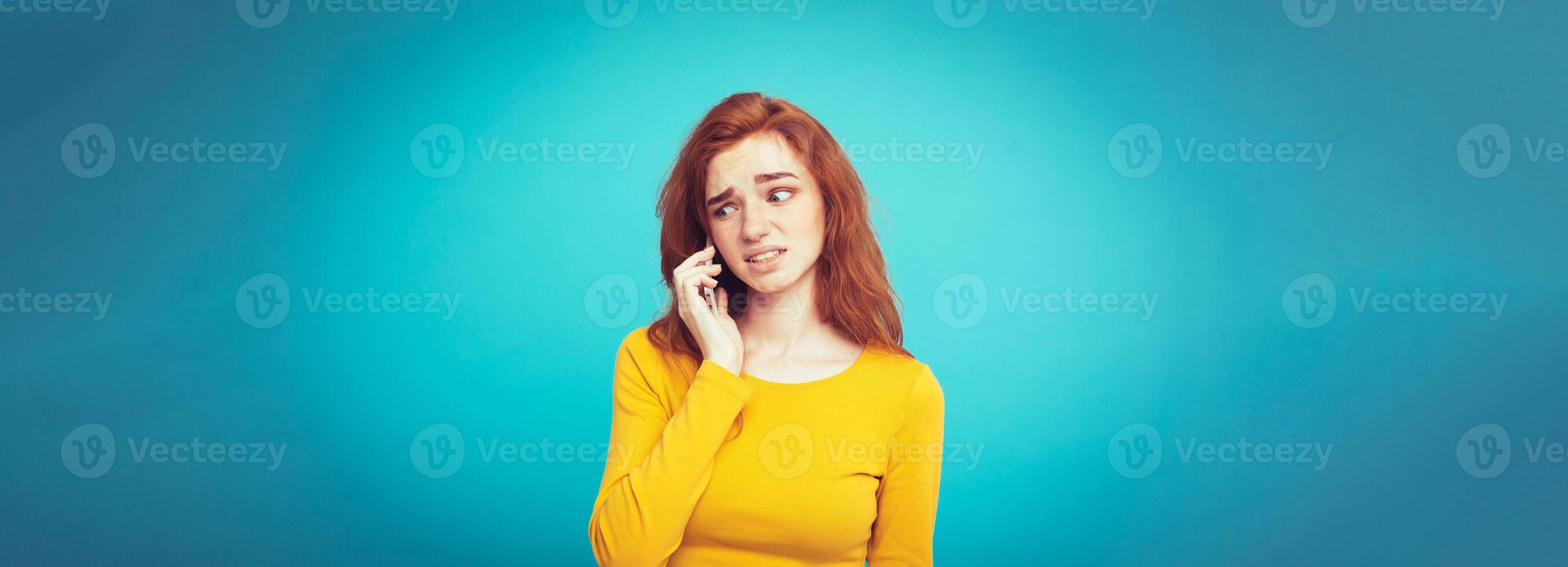 Lifestyle concept - Portrait of ginger red hair girl with shocking and stressful expression while talking with friend by mobile phone. Isolated on Blue Pastel Background. Copy space photo