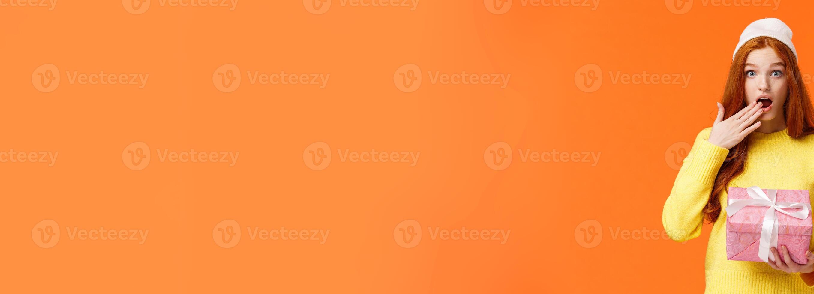 Girl surprised didnt expact gift from you. Amused and startled cute redhead girlfriend open mouth, cover it with hand as receive cute pink box of present, look camera excited, orange background photo