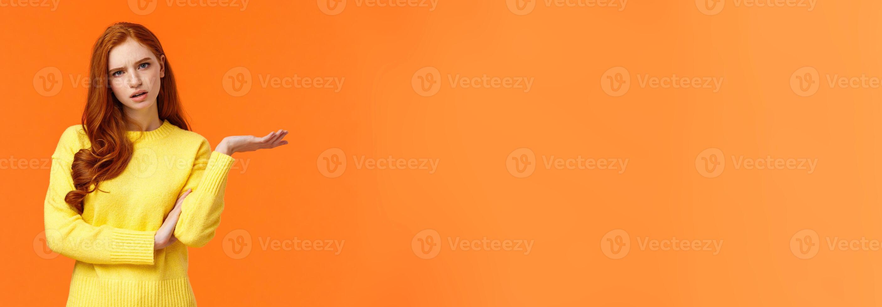 Skeptical and troubled, uncertain young redhead woman cant understand how resolve proble, shrugging raise hands sideways, frowning confused or unsure, standing frustrated orange background photo