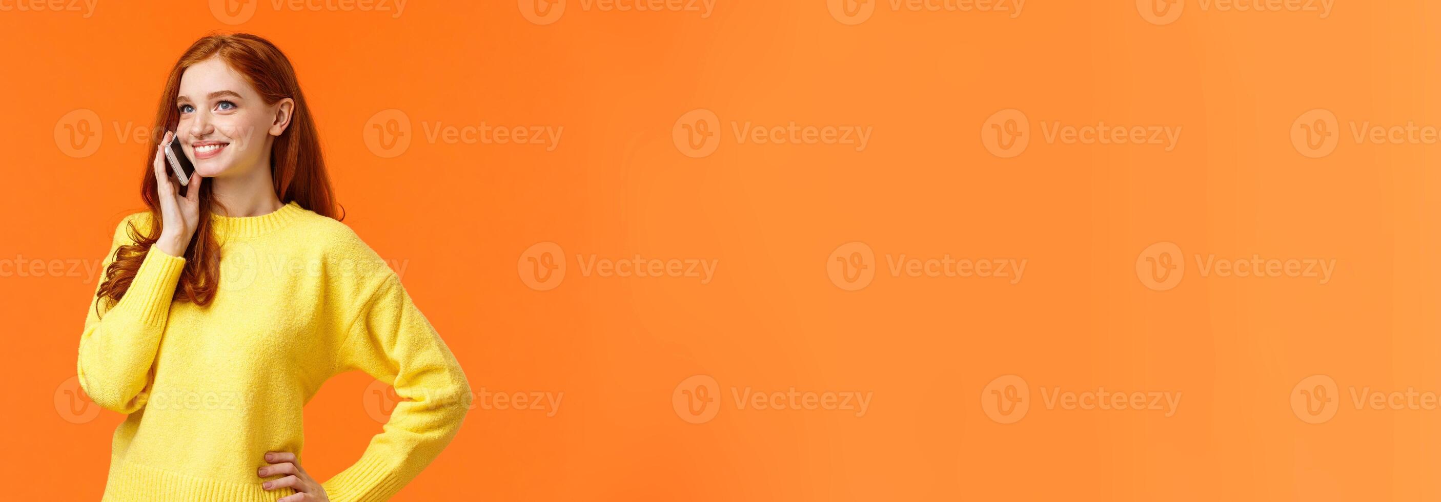 Waist-up portrait pretty redhead female calling friend, having conversation, confirm online order while shopping for holidays, standing carefree hold smartphone near ear, orange background photo