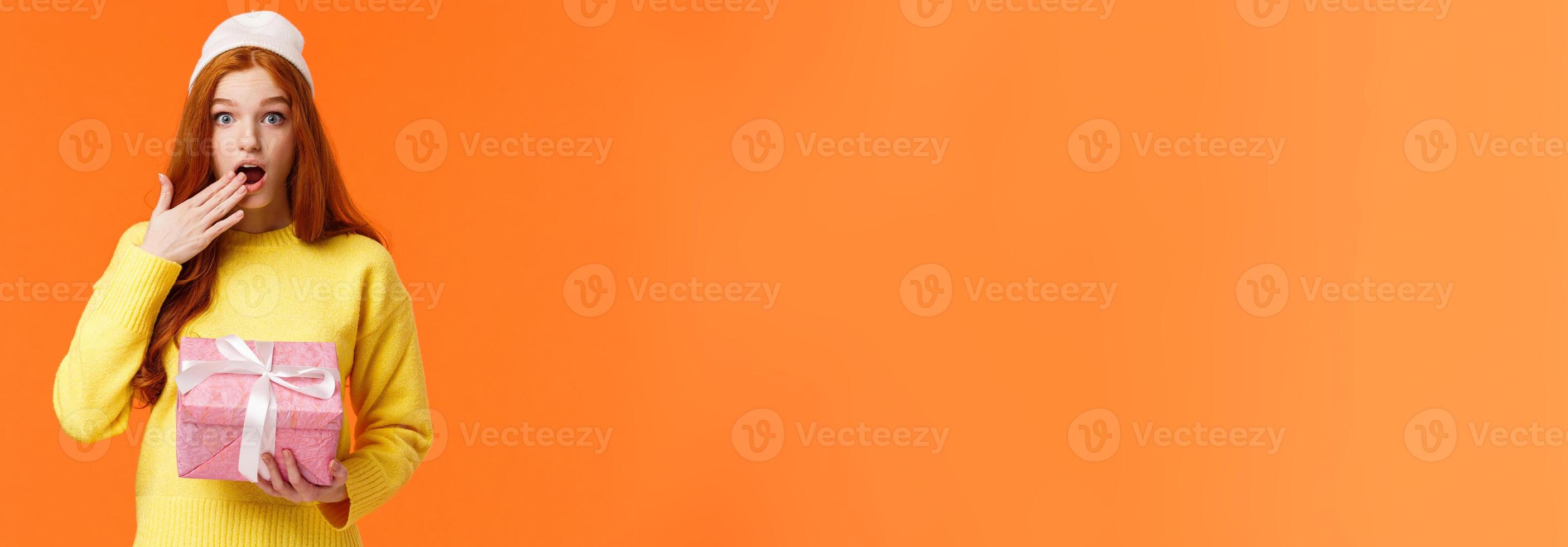 Girl surprised didnt expact gift from you. Amused and startled cute redhead girlfriend open mouth, cover it with hand as receive cute pink box of present, look camera excited, orange background photo