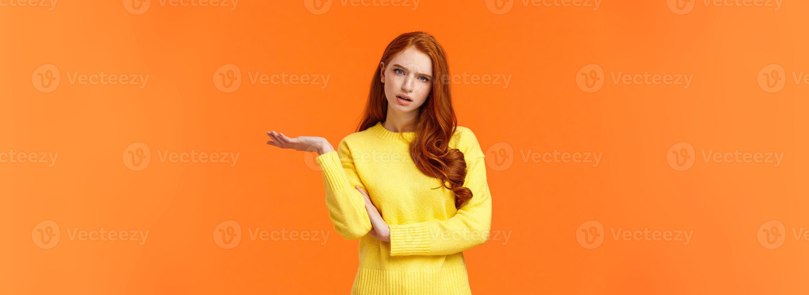 Skeptical and troubled, uncertain young redhead woman cant understand how resolve proble, shrugging raise hands sideways, frowning confused or unsure, standing frustrated orange background photo