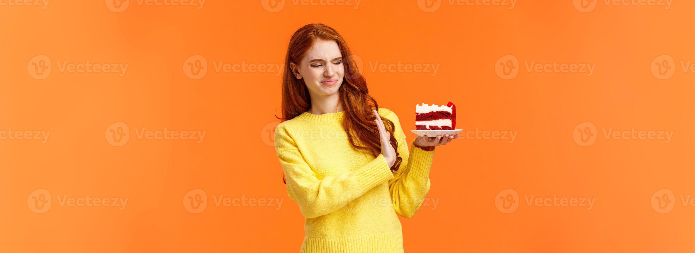 No thanks, dont want. Cute redhead girl trying resist temptation take bite delicious sweets, holding tasty cake and showing stop, refusal or rejection with grimacing face, express aversion, dislike photo